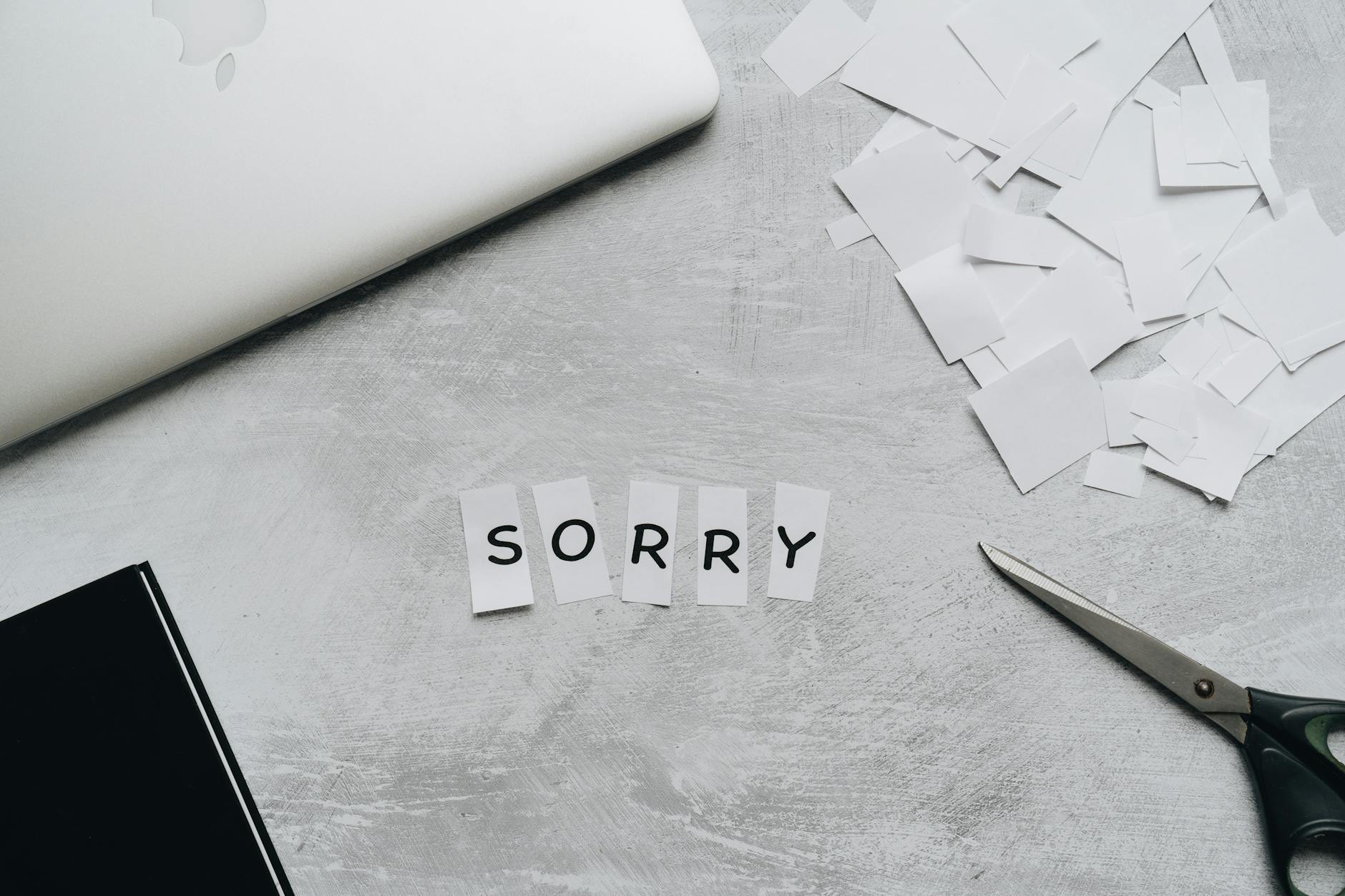 Top view of a desk with cut-out letters spelling 'sorry', scissors, and a laptop. - how to apologize to girlfriend