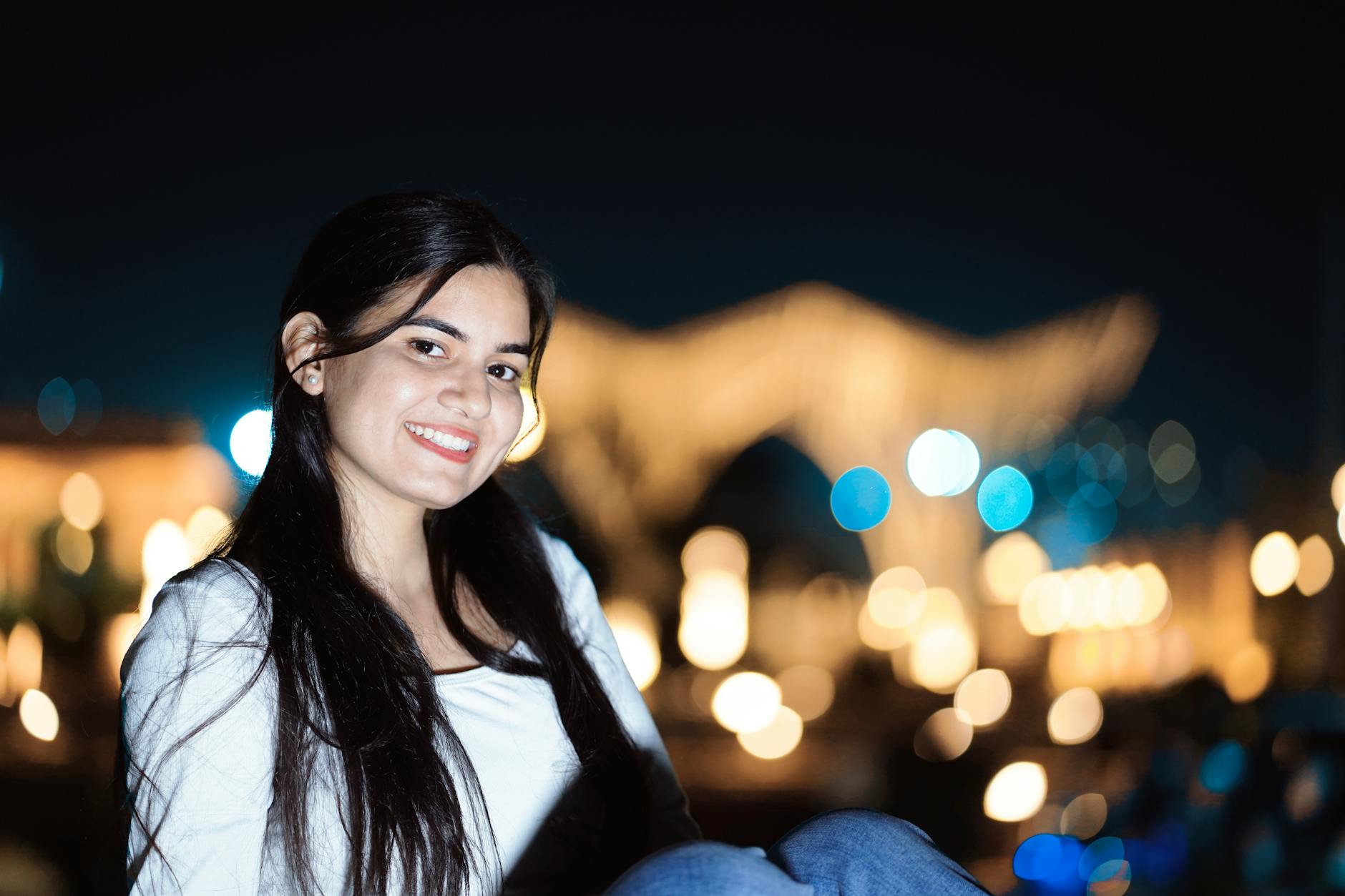 A young woman smiling against a blurry city lights backdrop at night. - how to apologize to girlfriend