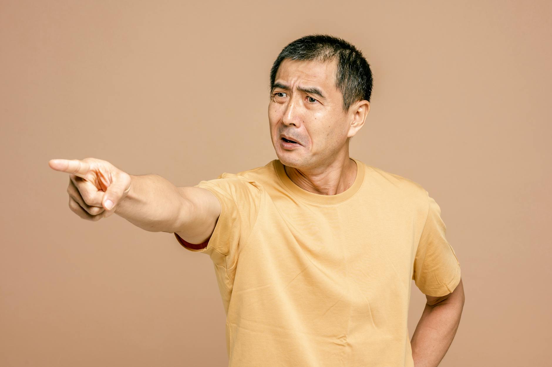 Senior Asian man expressing anger and pointing on a brown background. - assertive communication in conflict