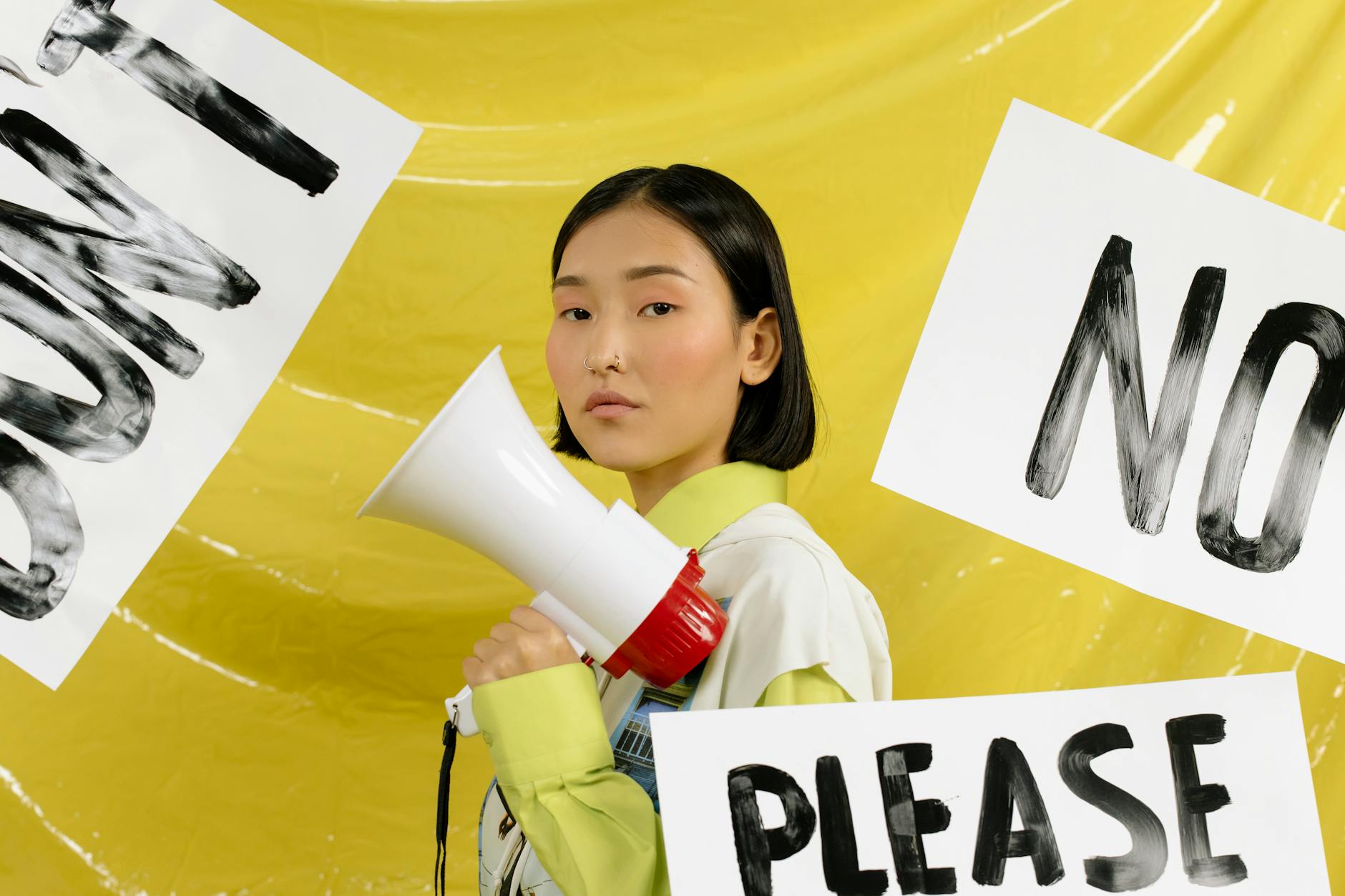 Portrait of a young activist holding a megaphone against a yellow background surrounded by protest signs. - assertive communication in conflict