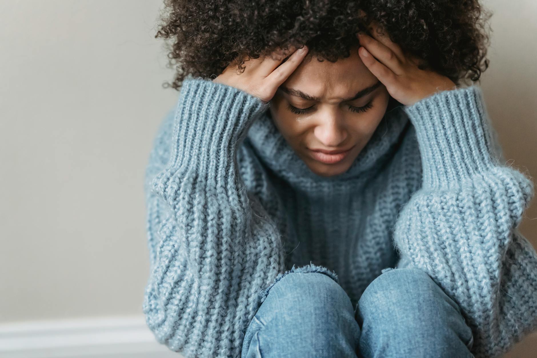 Young woman with curly hair looks thoughtful and pensive, wearing a cozy sweater indoors. - cbt for winter depression