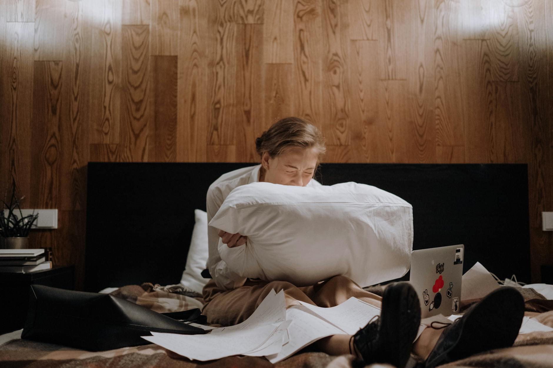 A woman sits alone on a bed, deep in thought, surrounded by papers and using a laptop. - cbt for winter depression