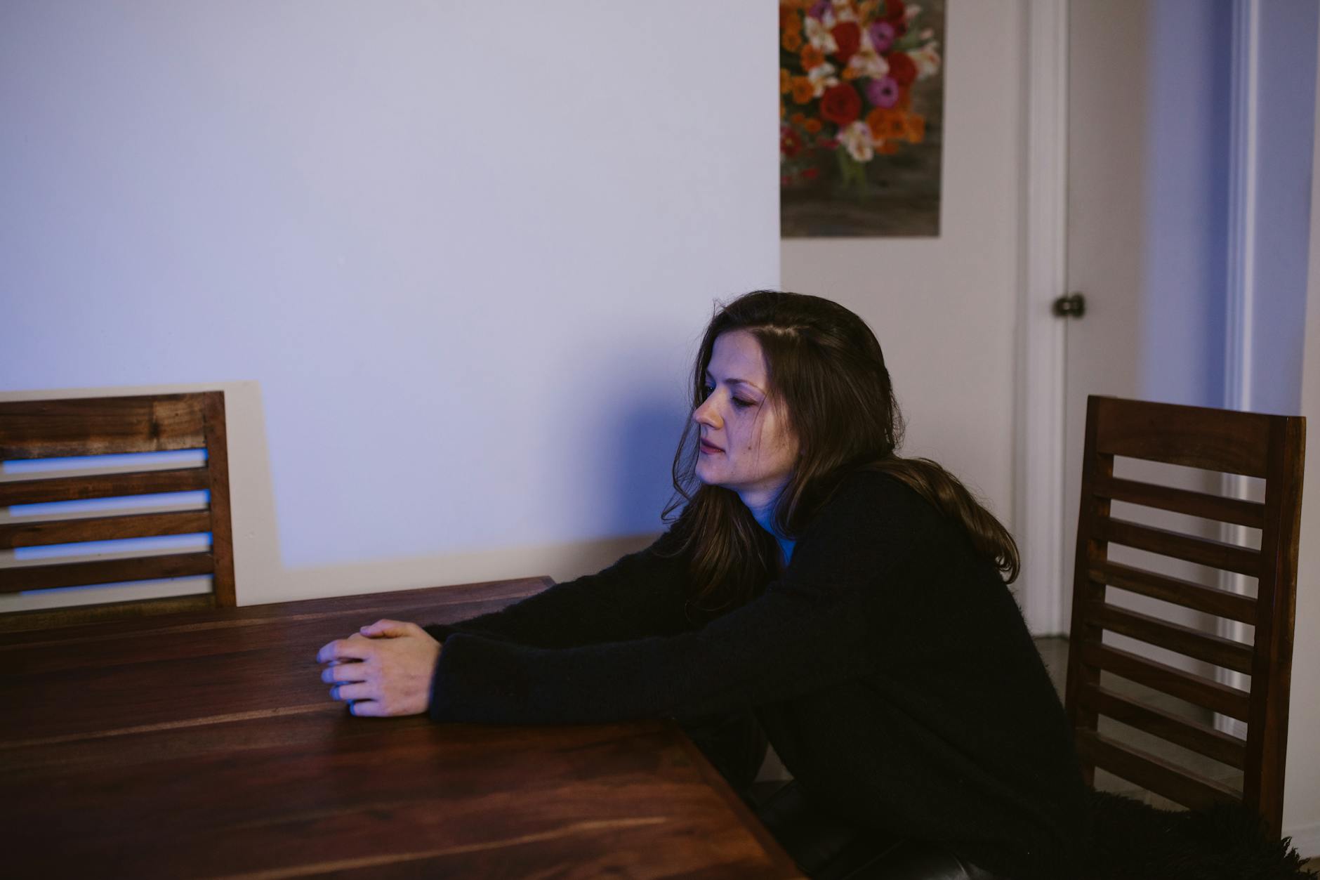 Woman sitting alone at a dining table, contemplating in a dimly lit room. - cbt for winter depression
