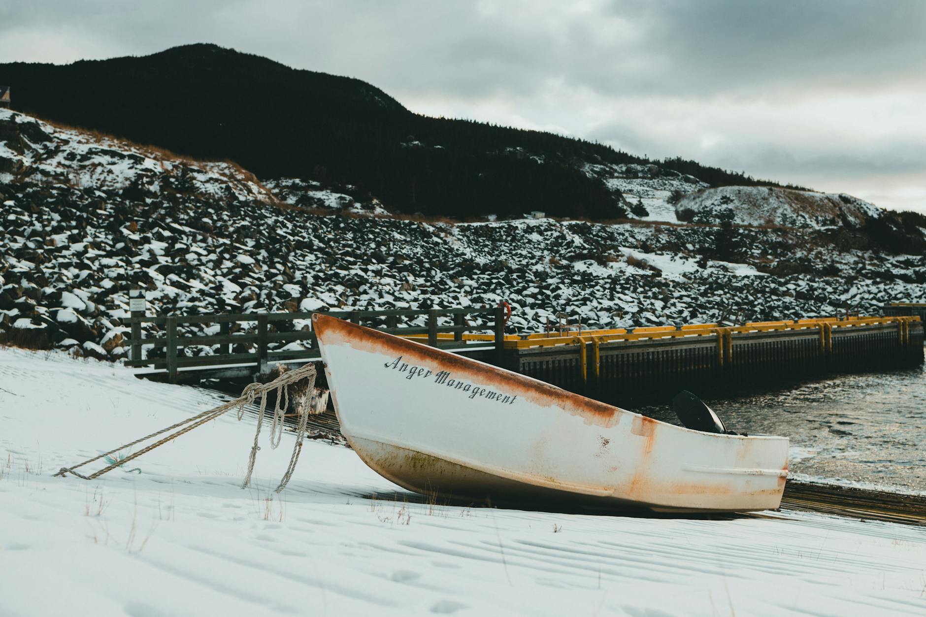 Rustic boat named 'Anger Management' resting on snowy shore by a rocky landscape. - celebrity anger management lessons