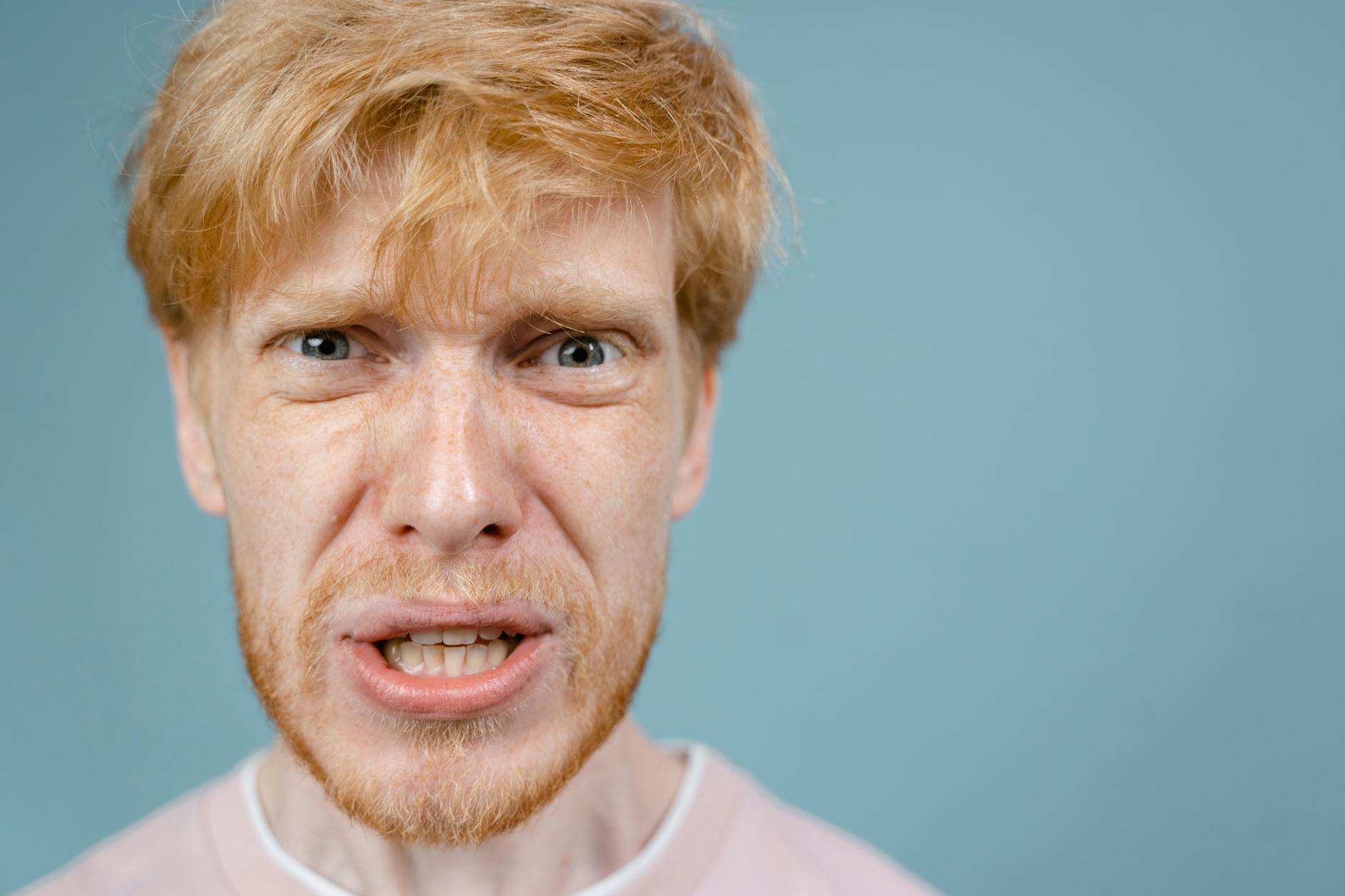 Close-up of a redhead man showing an intense facial expression against a blue background. - celebrity anger management lessons