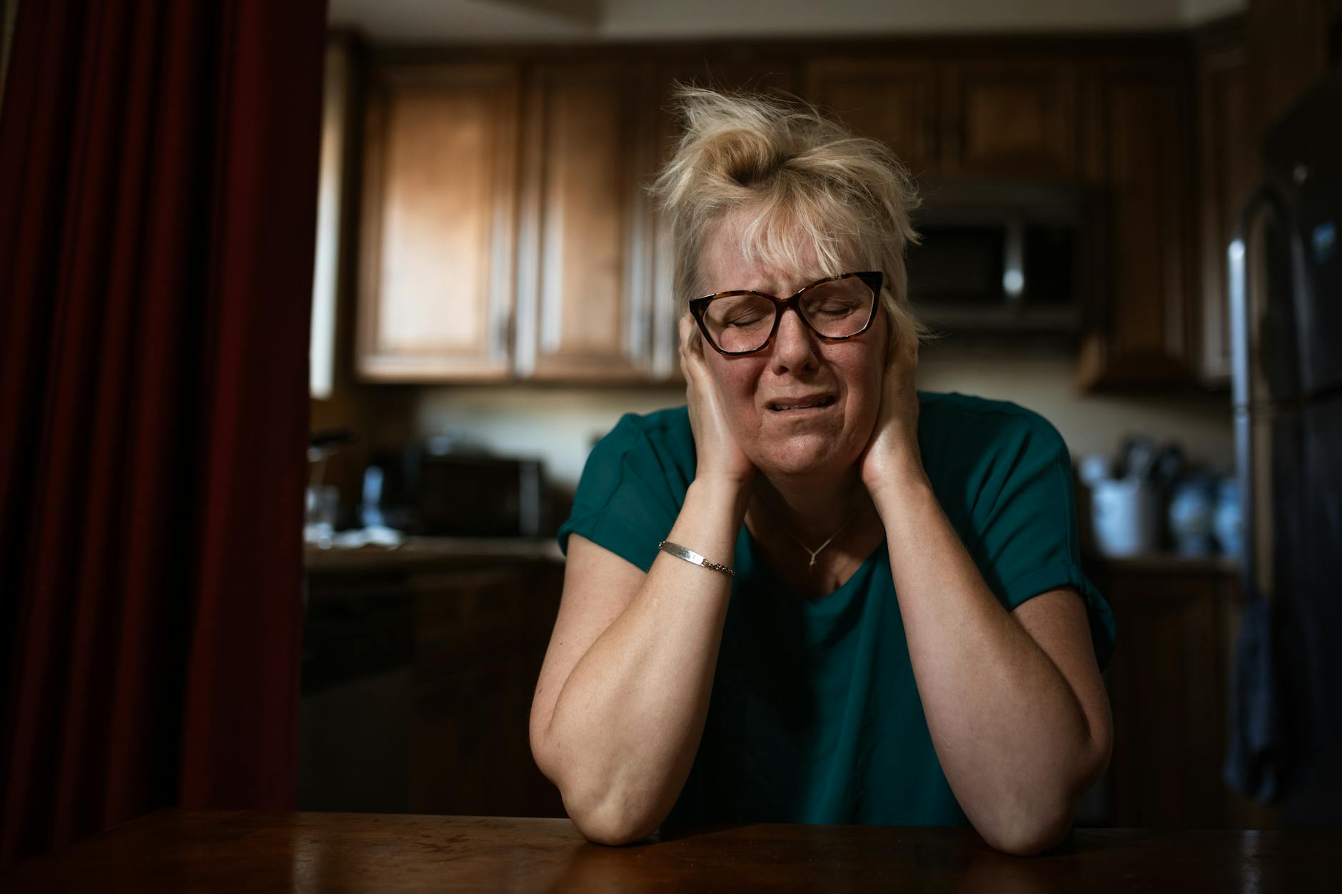 An adult woman in distress sitting at a table indoors, conveying emotional struggle. - charlie sheen mental health struggles