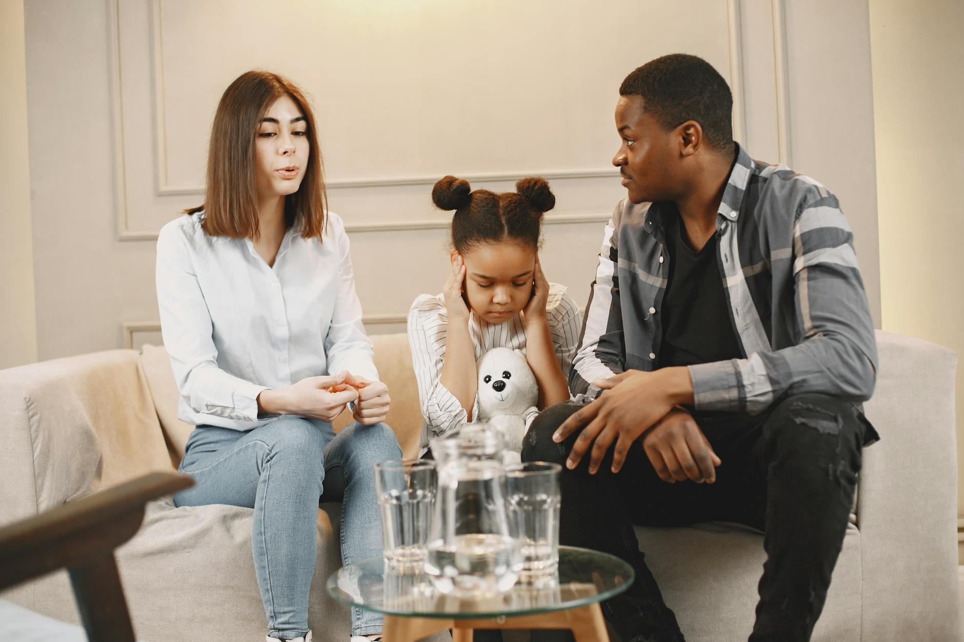 Parents talking to daughter covering ears on sofa. - child social emotional development break