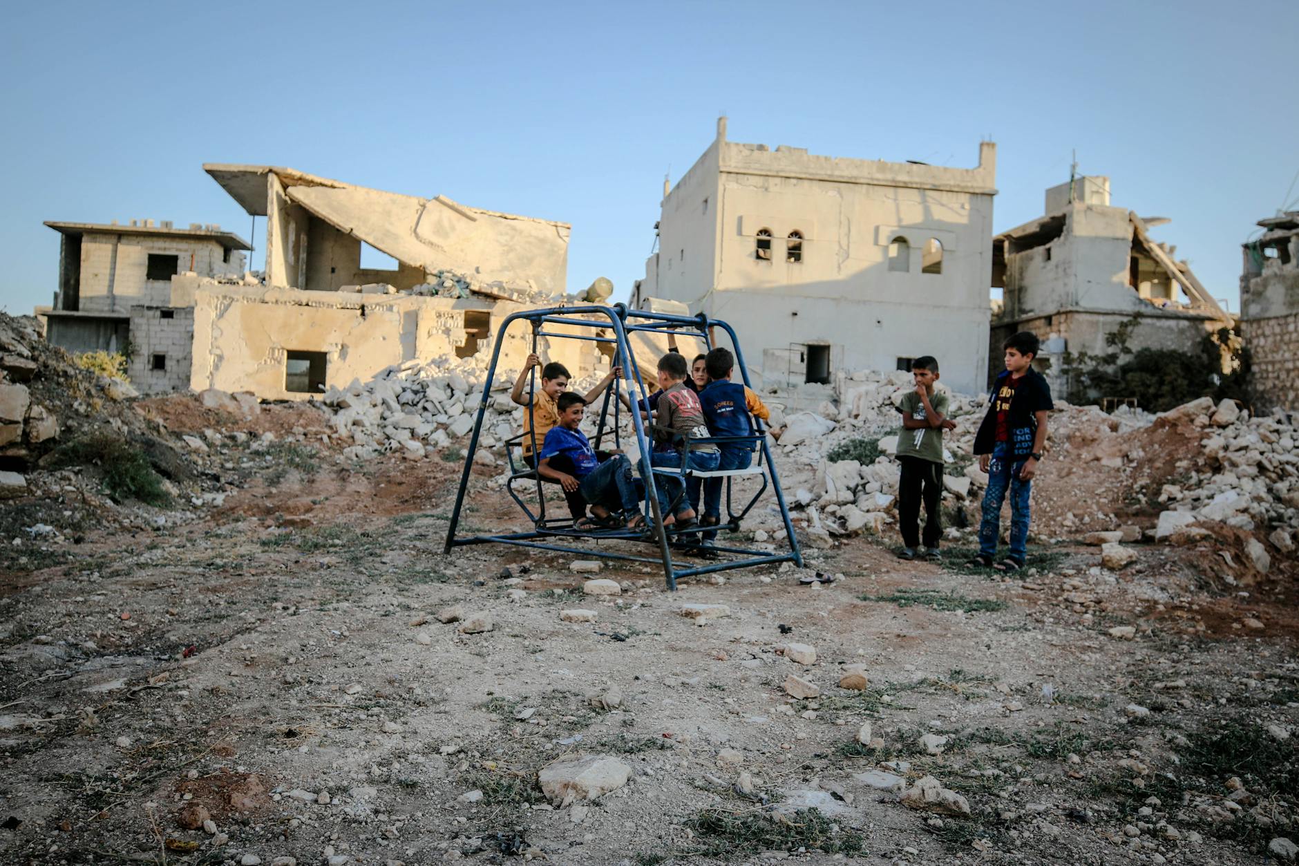 Syrian children play on a swing amidst the decaying ruins of Idlib after conflict. - childhood trauma symptoms
