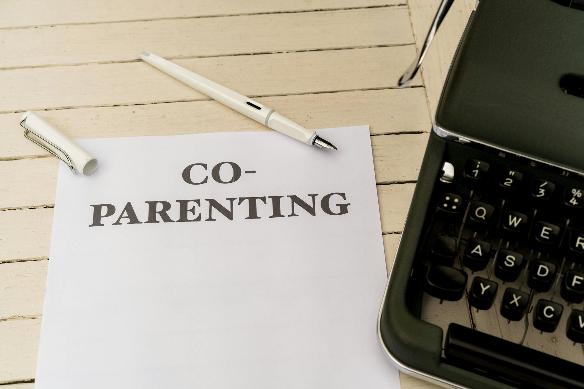Co-parenting paper and pen on a white wooden table next to a typewriter. - co-parenting communication winter break
