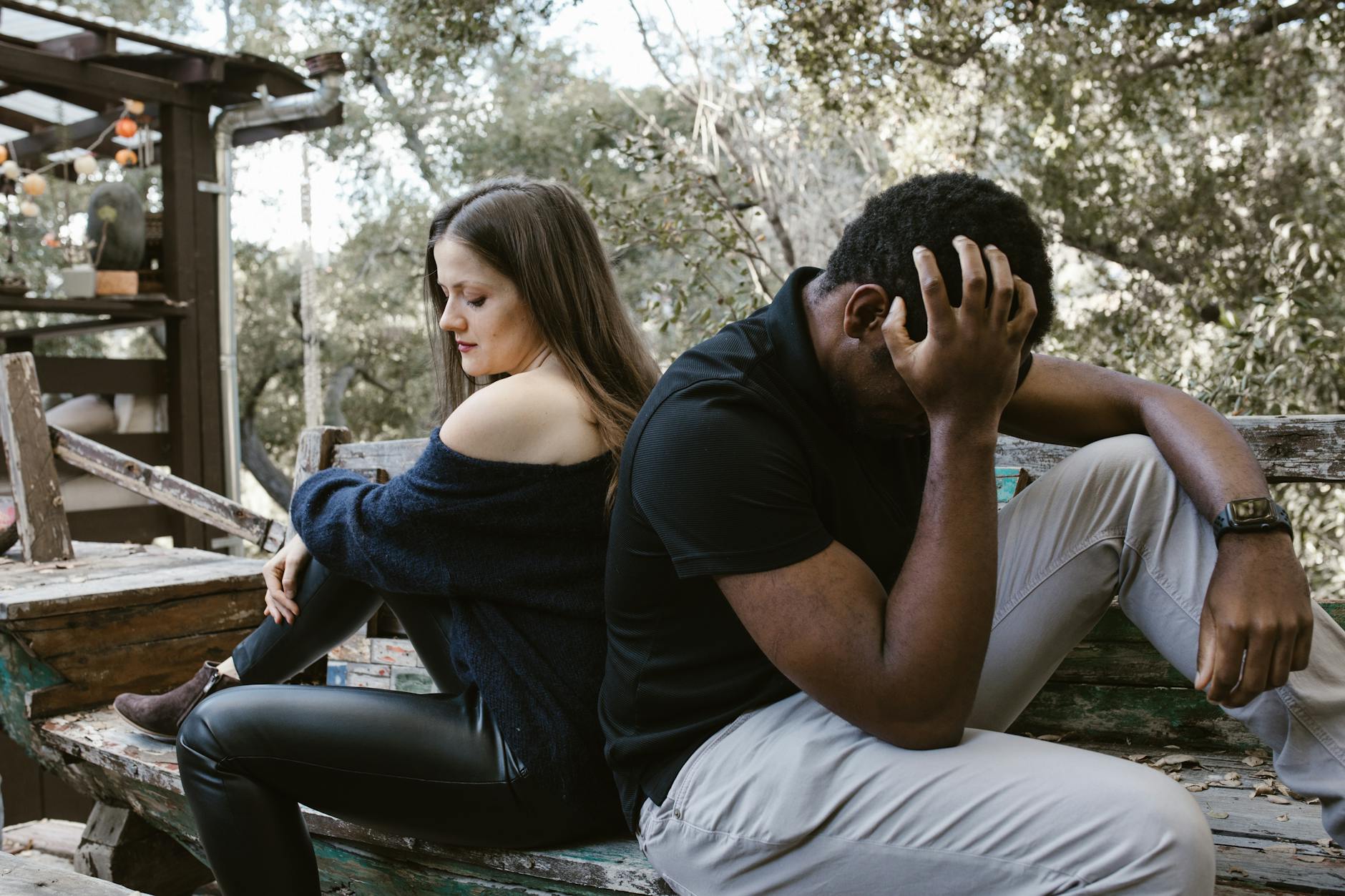 A couple sits back to back on a bench, depicting emotional conflict and loneliness. - how to cope with breakup