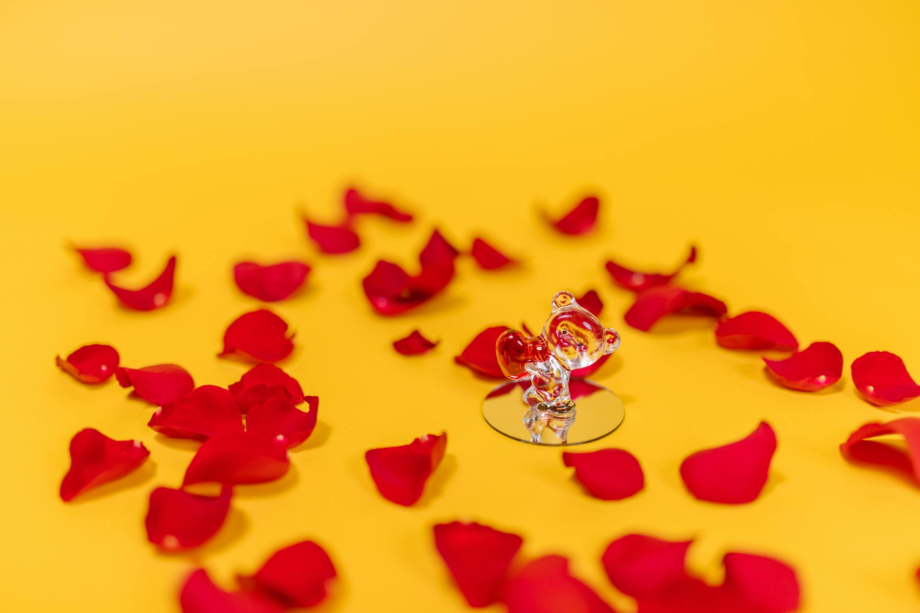 Glass figurine surrounded by red rose petals on a vibrant yellow background, symbolizing love and romance. - creative valentine's day ideas