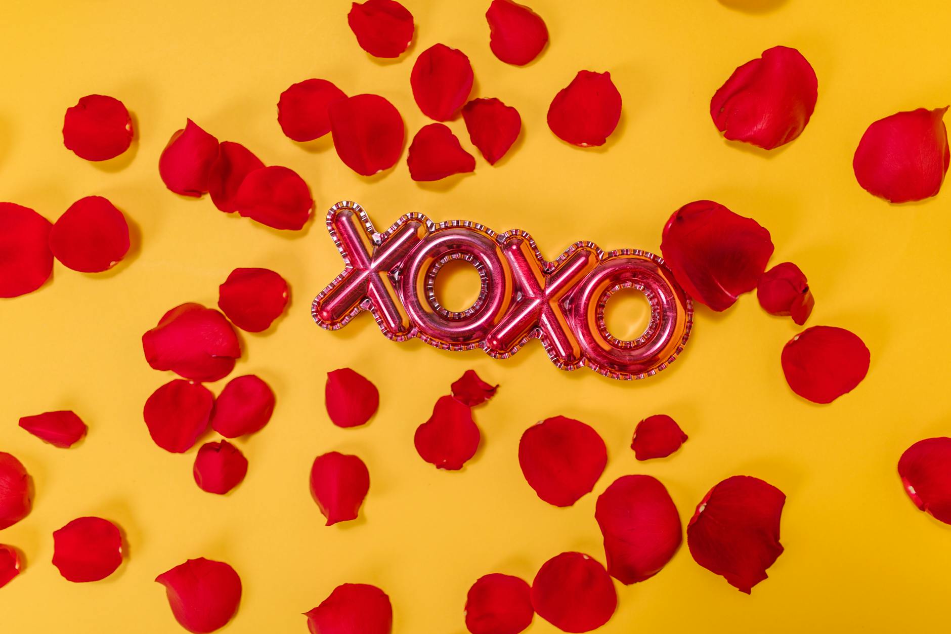 Red rose petals and xoxo letters on a vibrant yellow backdrop symbolizing love and romance. - creative valentine's day ideas