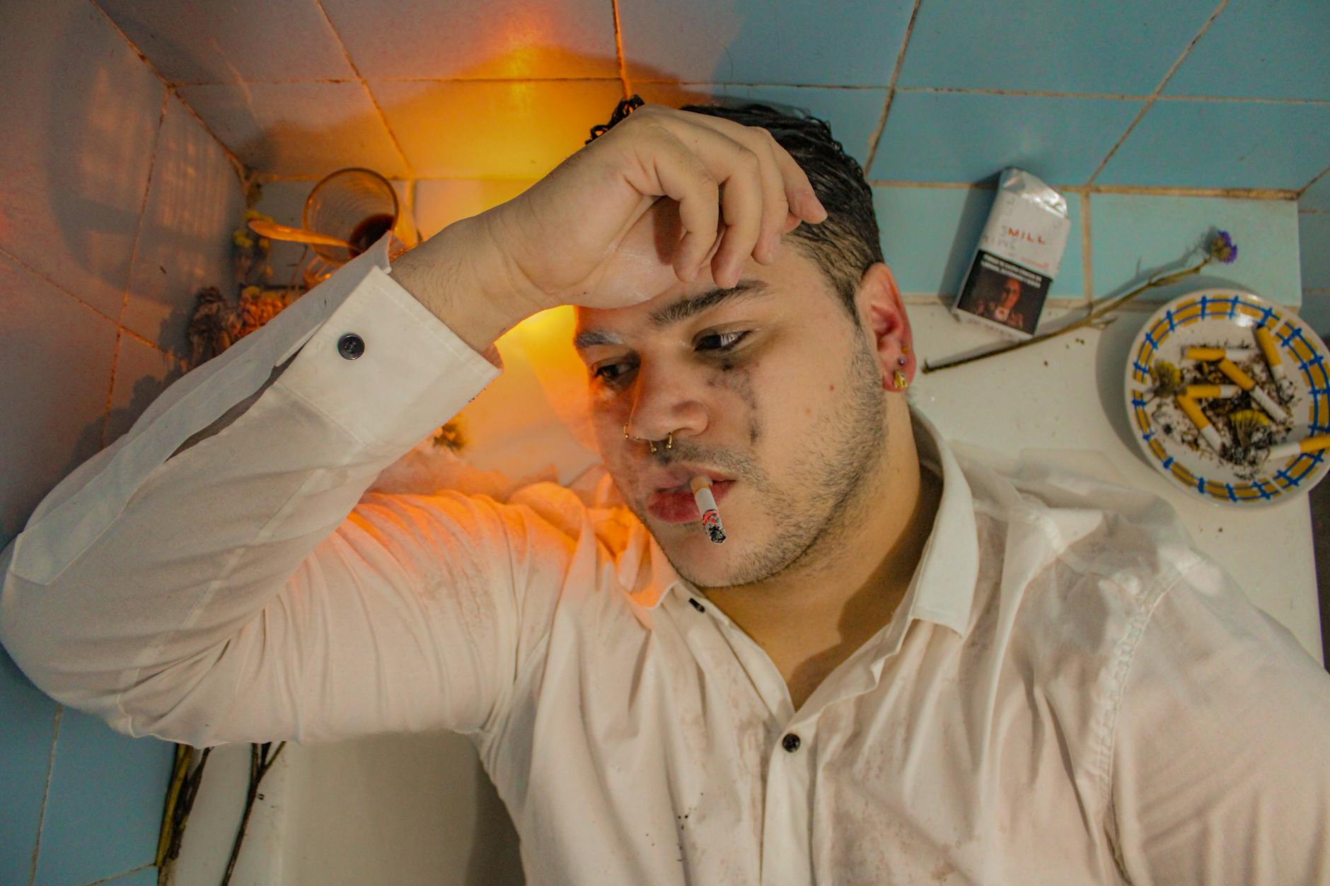 A young man in a white shirt smokes in a bathtub, expressing melancholy. - depression coping mechanisms