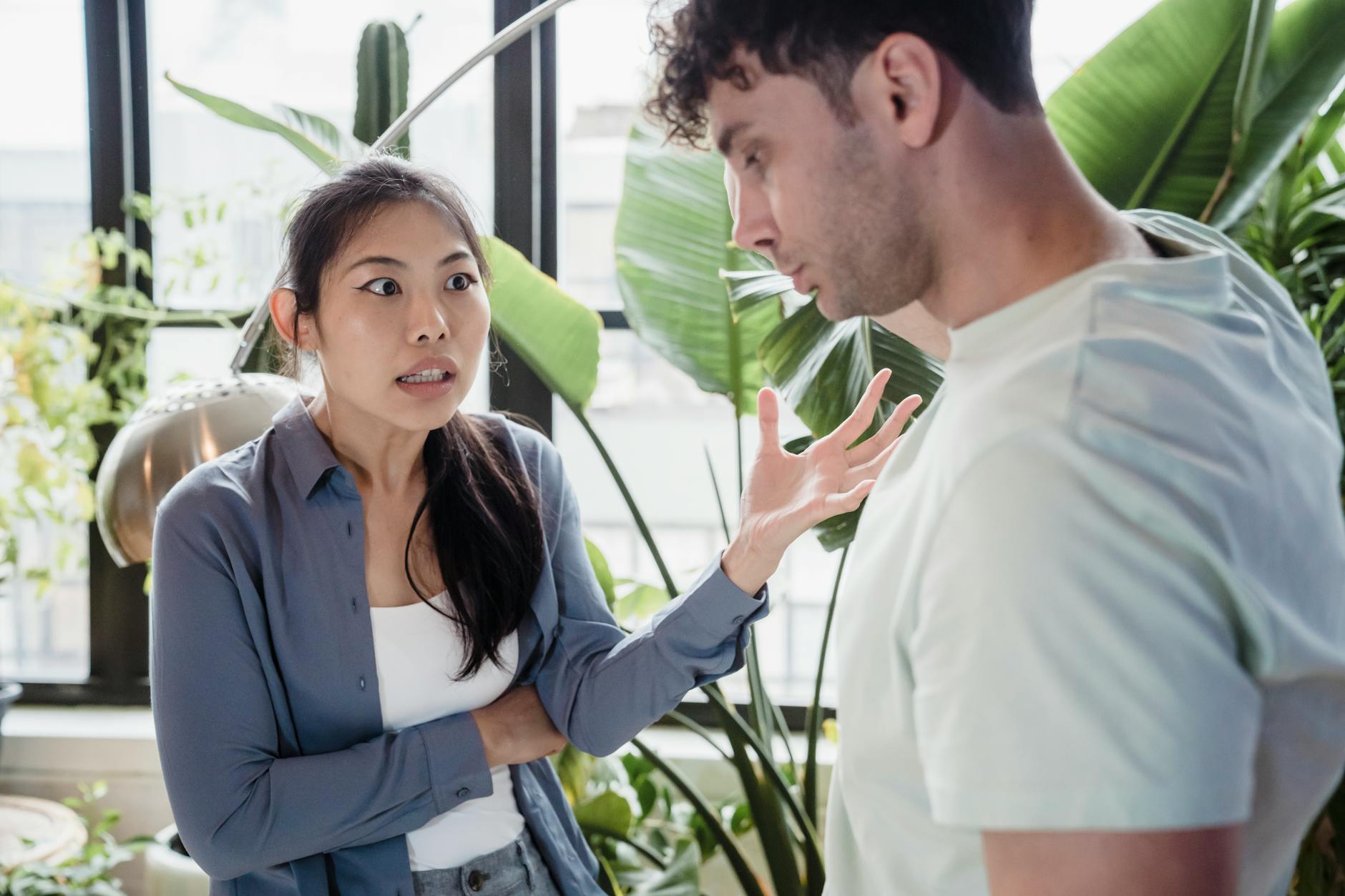 A couple engaged in a heated discussion indoors surrounded by plants, expressing emotions. - effective relationship communication skills