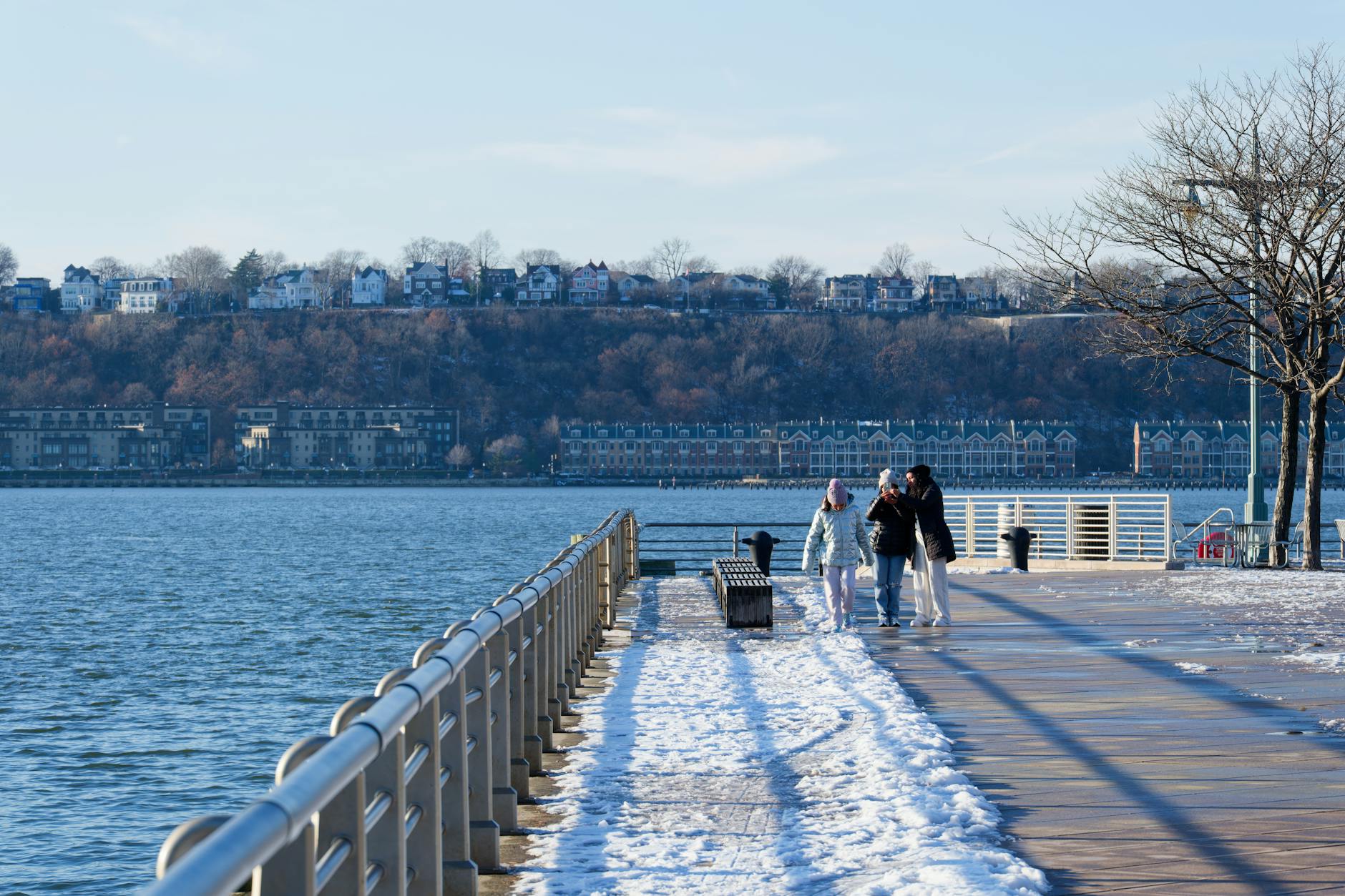 A serene family walk on a snow-covered boardwalk with scenic river views in New York City. - family snow day communication