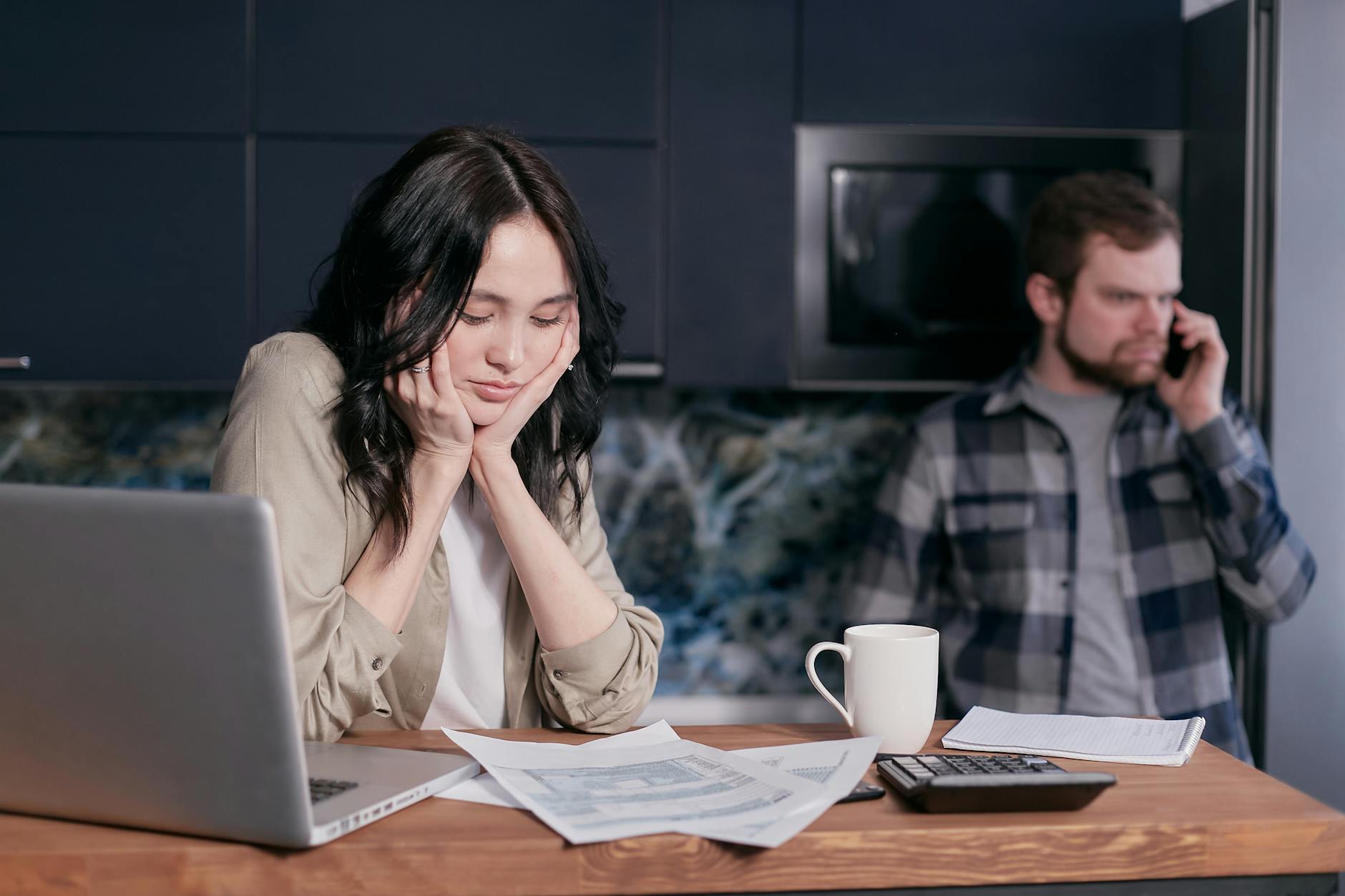 Couple dealing with financial stress at home, surrounded by bills and a laptop. - holiday financial stress relationships