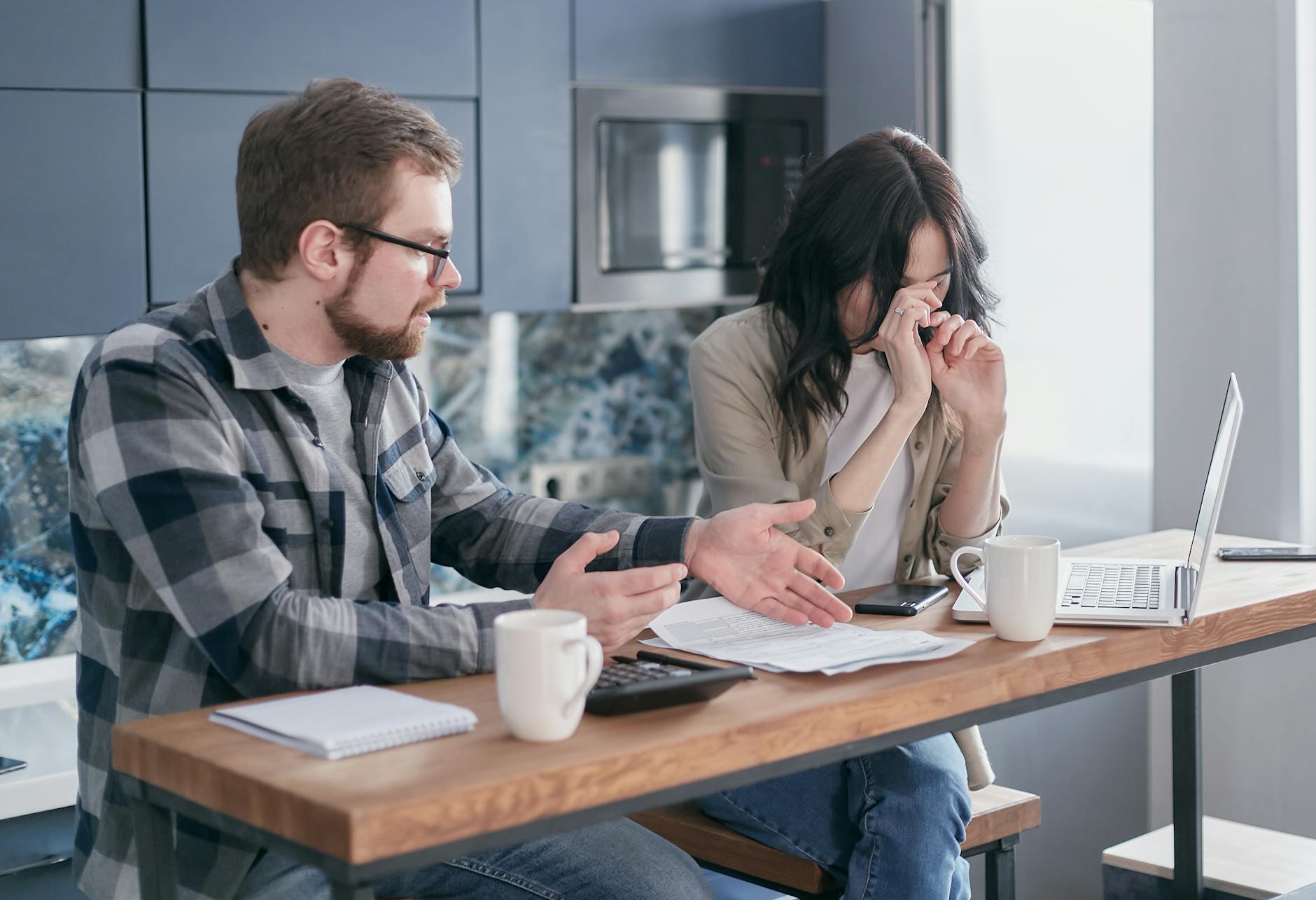 A couple sitting at a table indoors, visibly stressed while discussing bills and finances. - holiday financial stress relationships