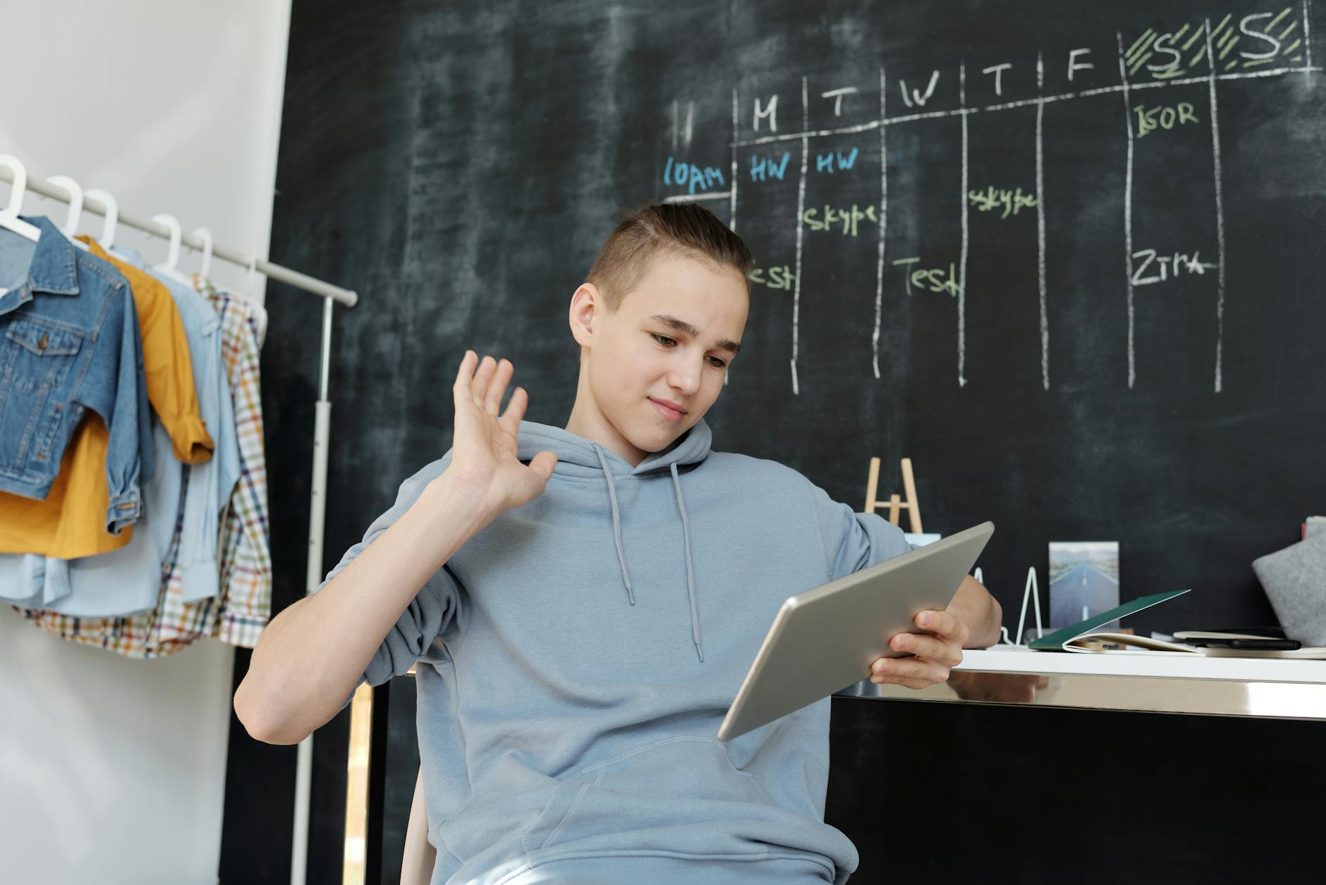 A teenager uses a tablet for online learning in a cozy home setting, waving at the screen. - improving teen communication at home