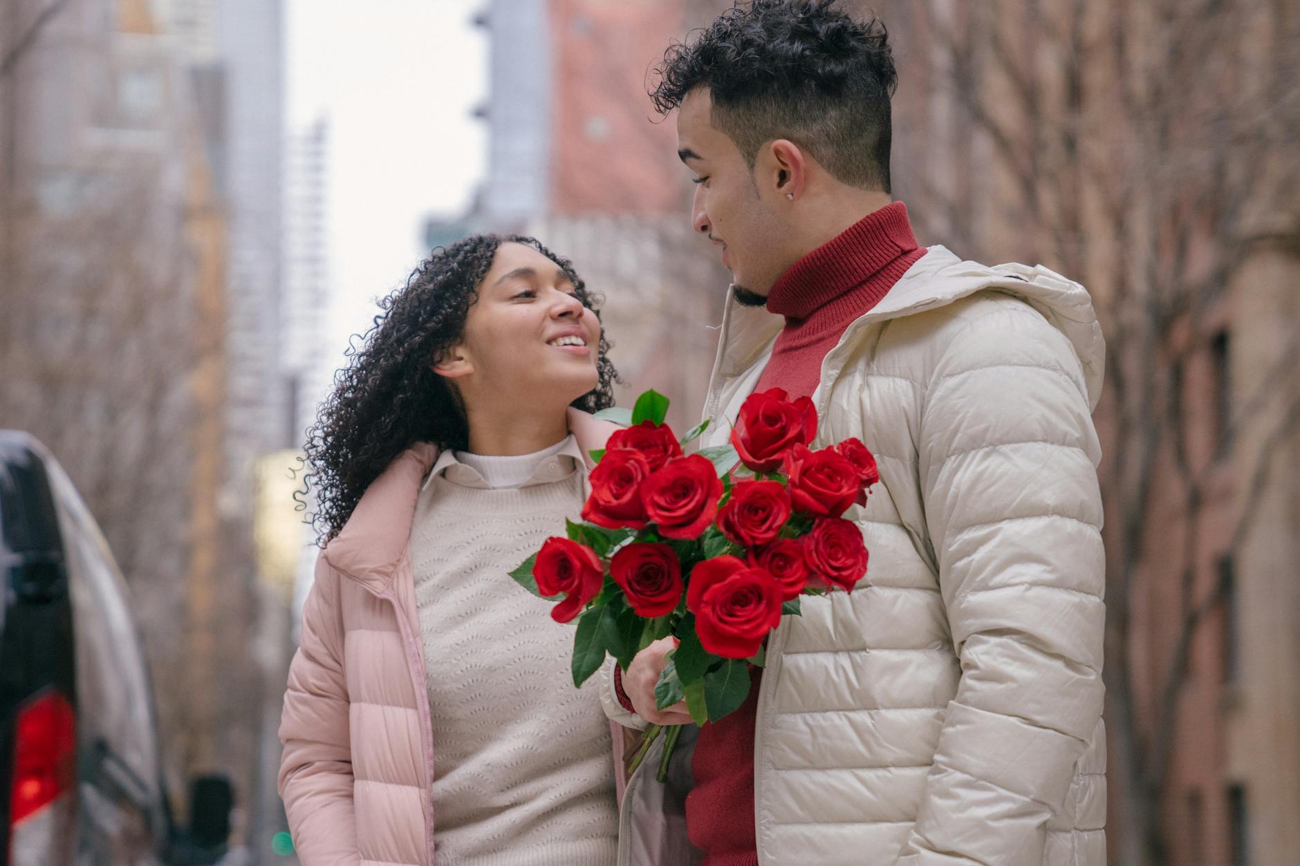 A couple shares a romantic moment with red roses on a city street during winter. - intimate winter date ideas