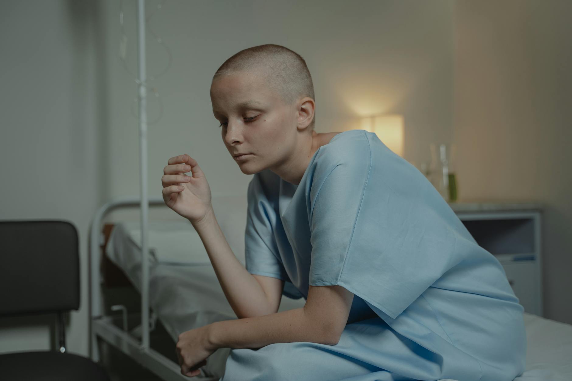 Bald woman sitting in a hospital gown, depicting sadness and contemplation. - latest postpartum depression treatments