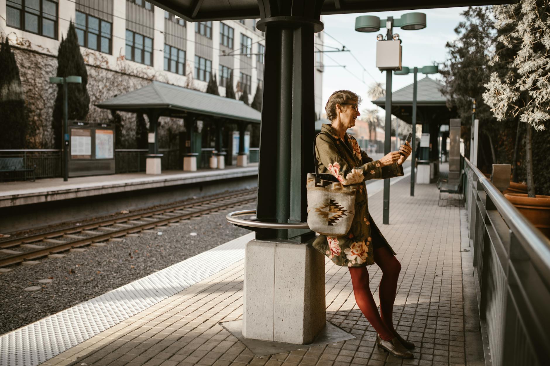 Stylish woman using smartphone at urban train station on a sunny day. - long distance winter travel