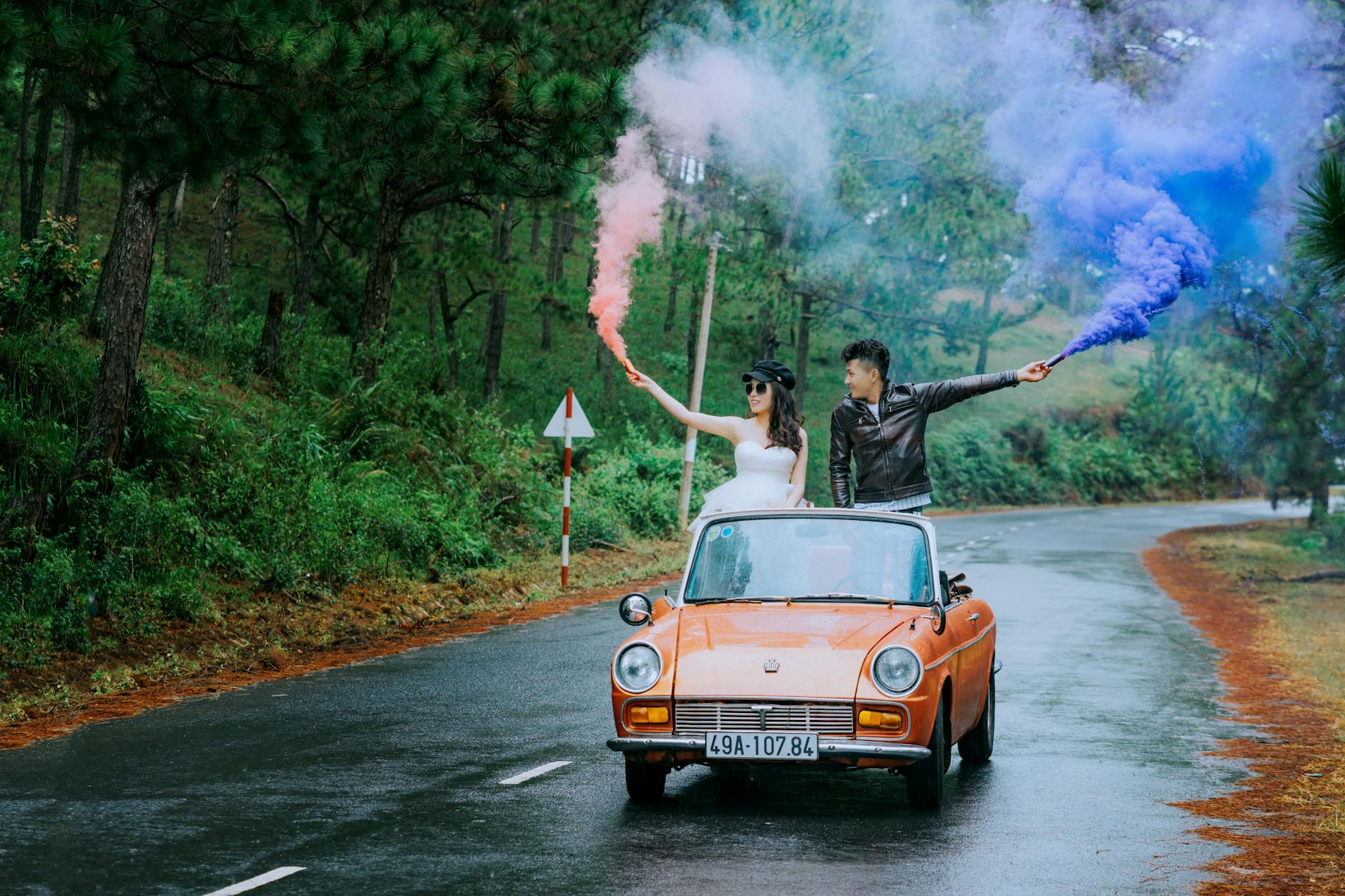 Young couple on a vibrant road trip in a vintage car, celebrating with colorful smoke bombs. - love bombing meaning