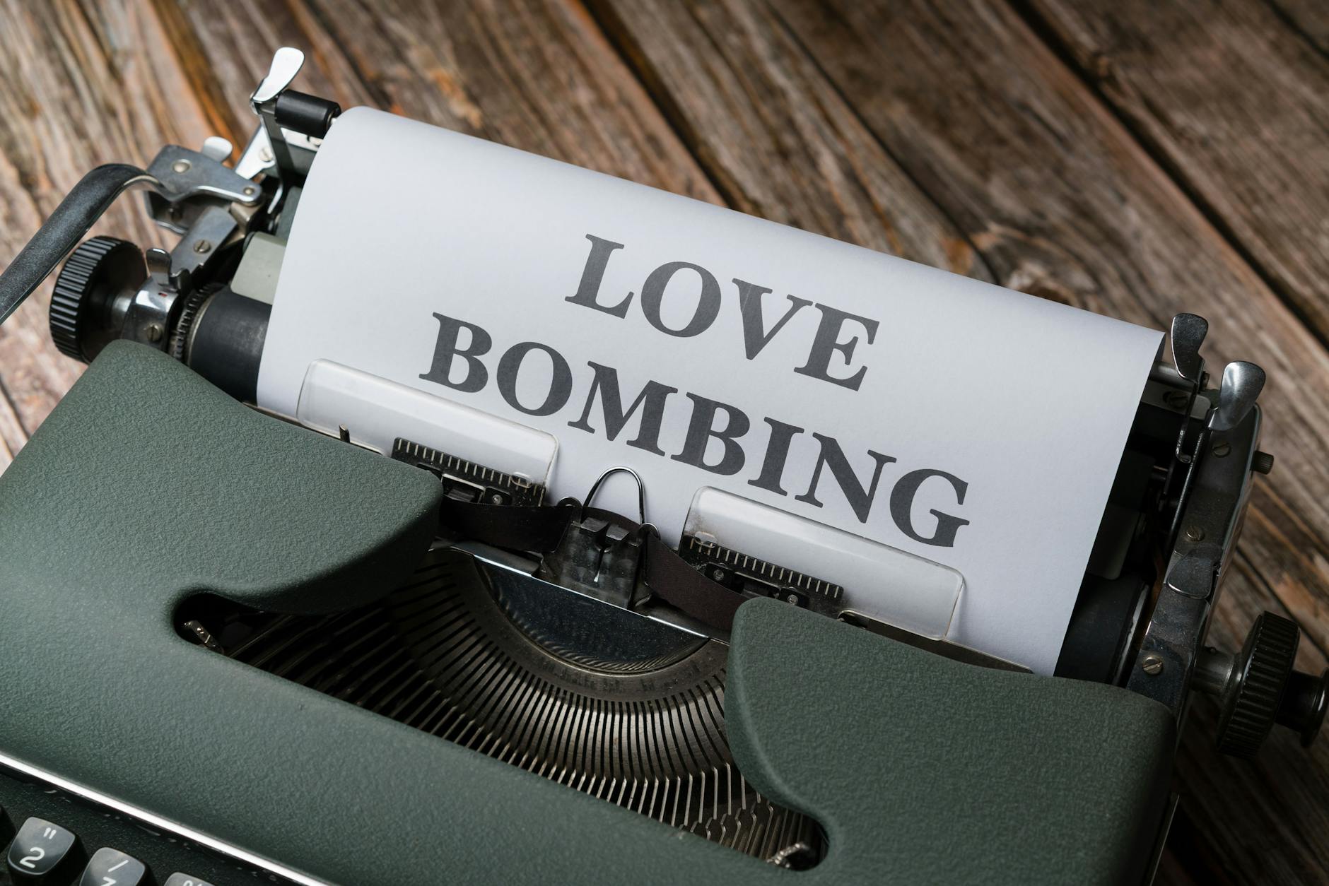 Close-up of a vintage typewriter printing 'Love Bombing' on paper, placed on a wooden desk. - narcissistic relationship signs