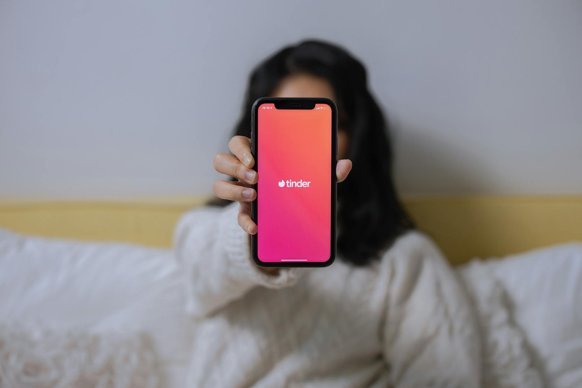 A woman in casual attire displays the Tinder app on her smartphone while sitting indoors. - online dating tips men
