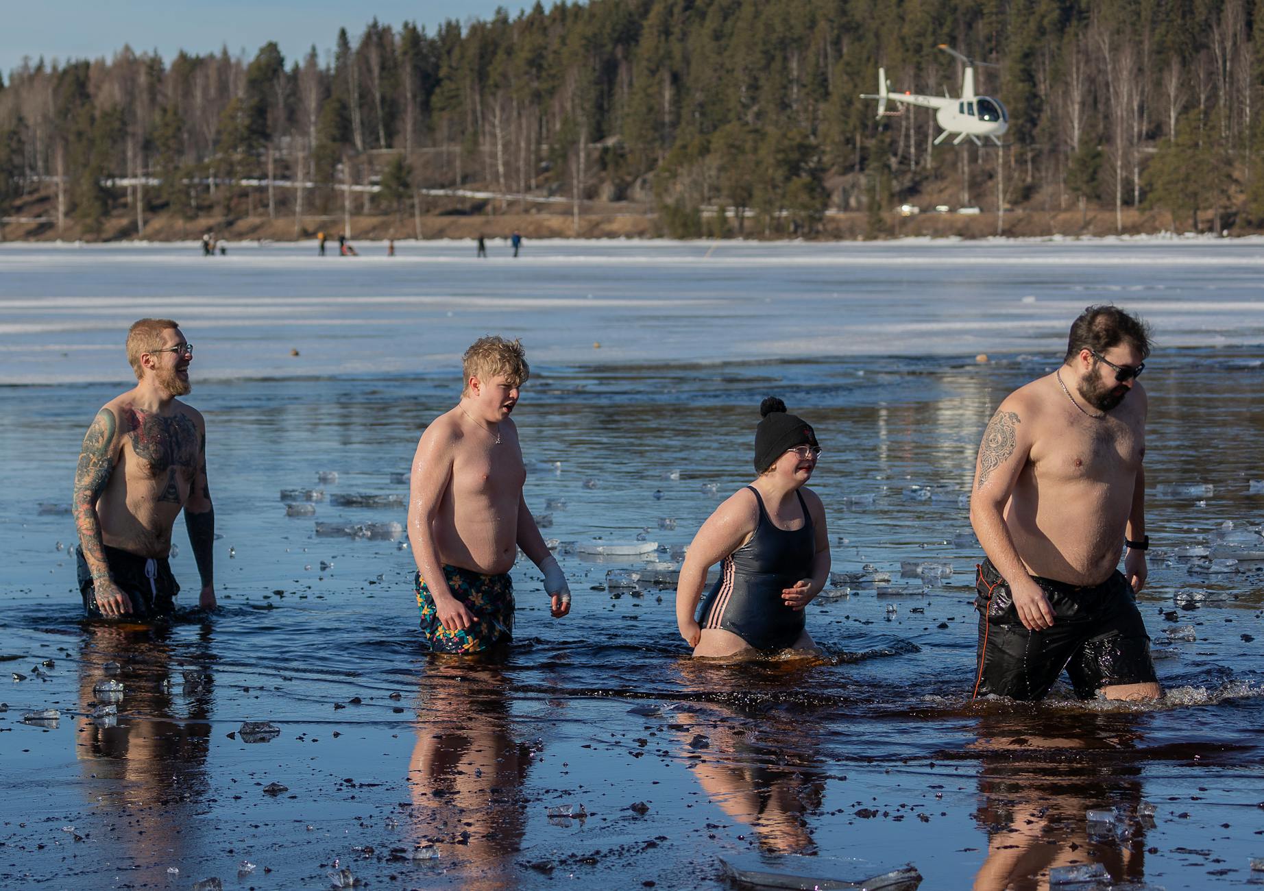 Four friends bravely plunge into a frozen lake, embracing the chilly adventure amid a winter landscape. - overcoming winter perfectionism