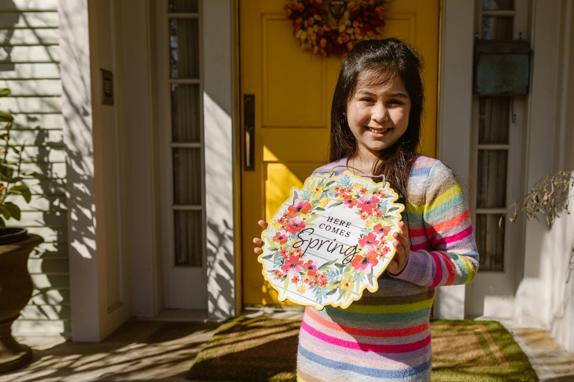 Smiling girl holding a vibrant spring decor sign at home entrance. - preparing kids for spring transition
