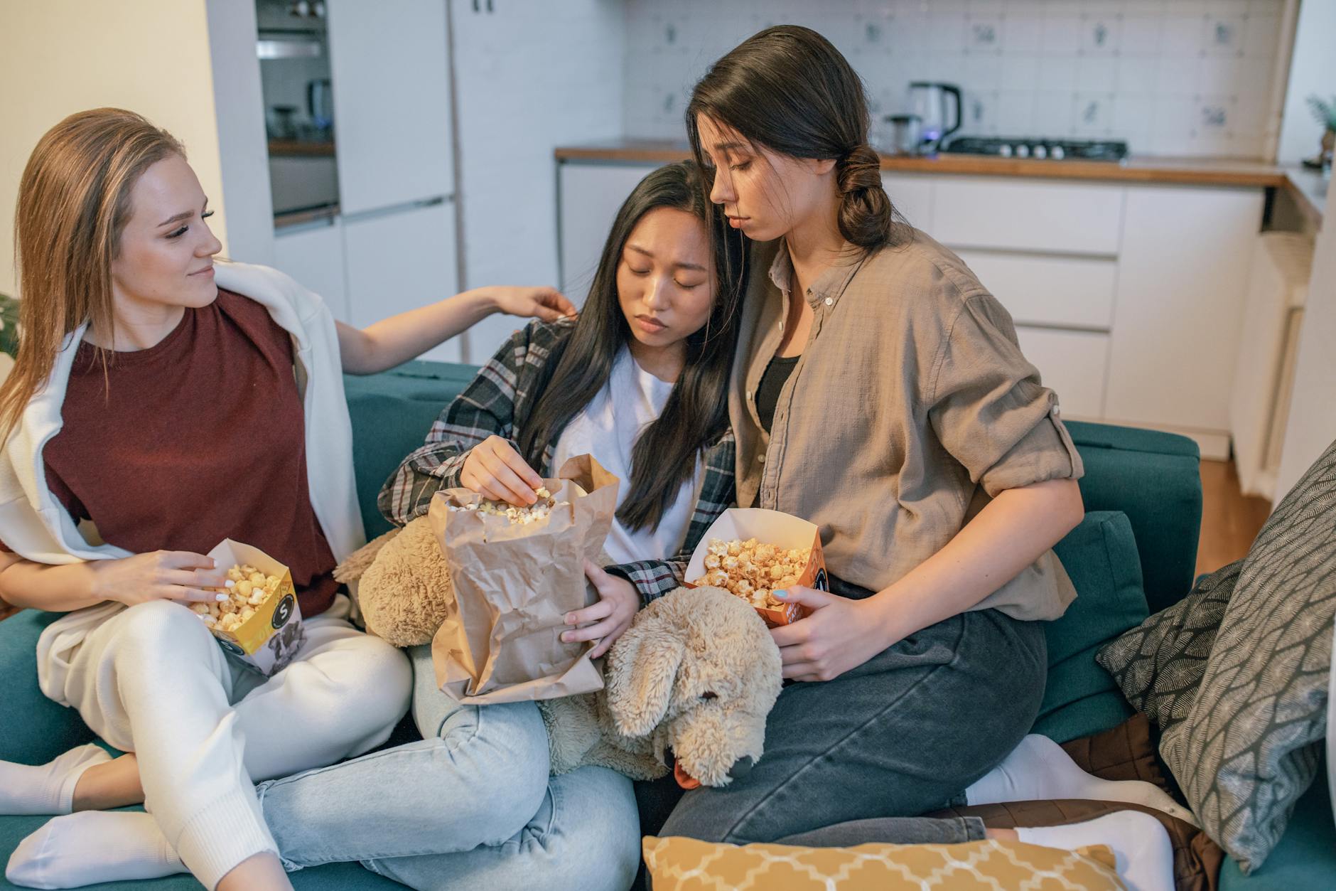 Three women share popcorn on a couch, bonding and offering support. An intimate, cozy moment indoors. - rebuilding trust after affair