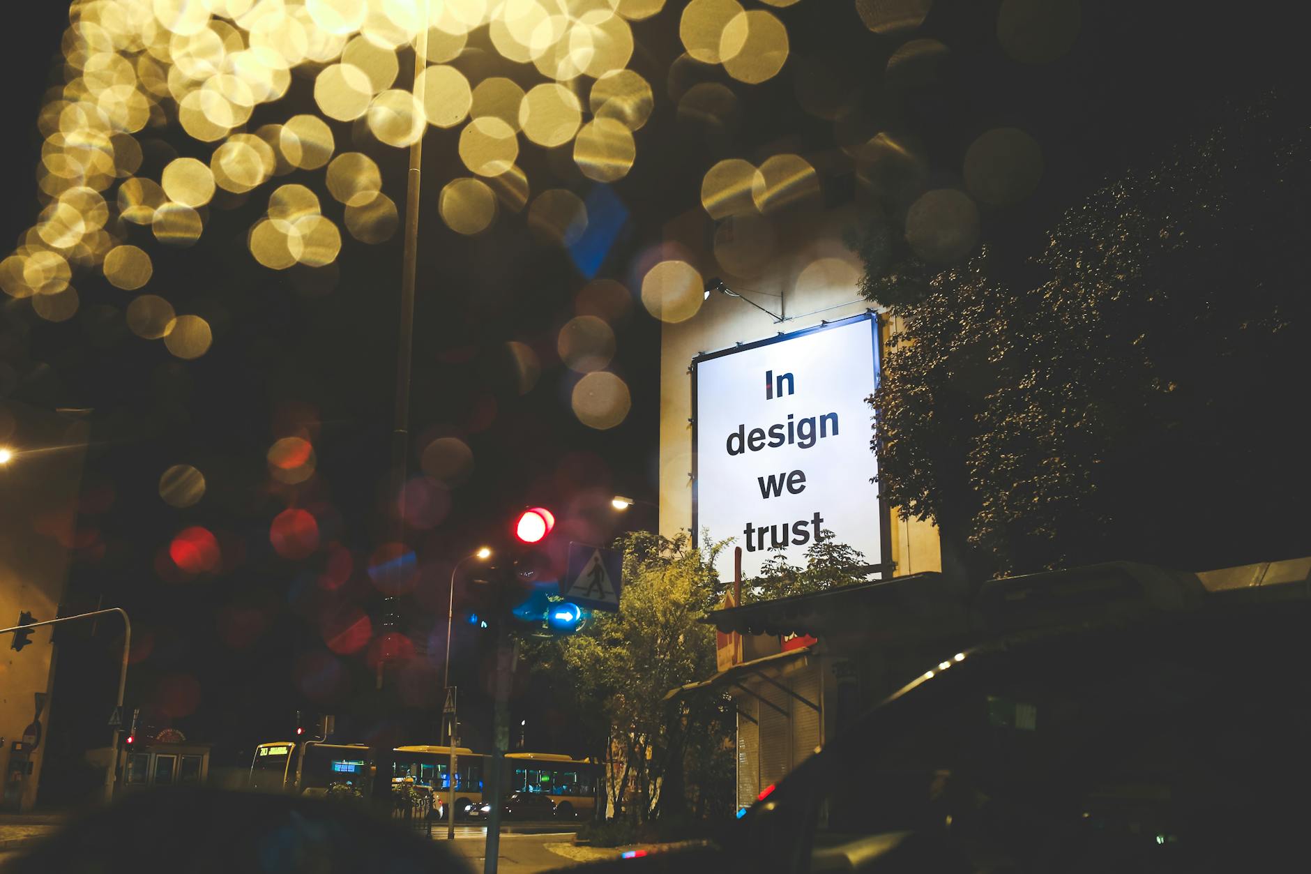 A city street at night featuring an illuminated billboard with the phrase 'In design we trust.' - rebuilding trust quotes