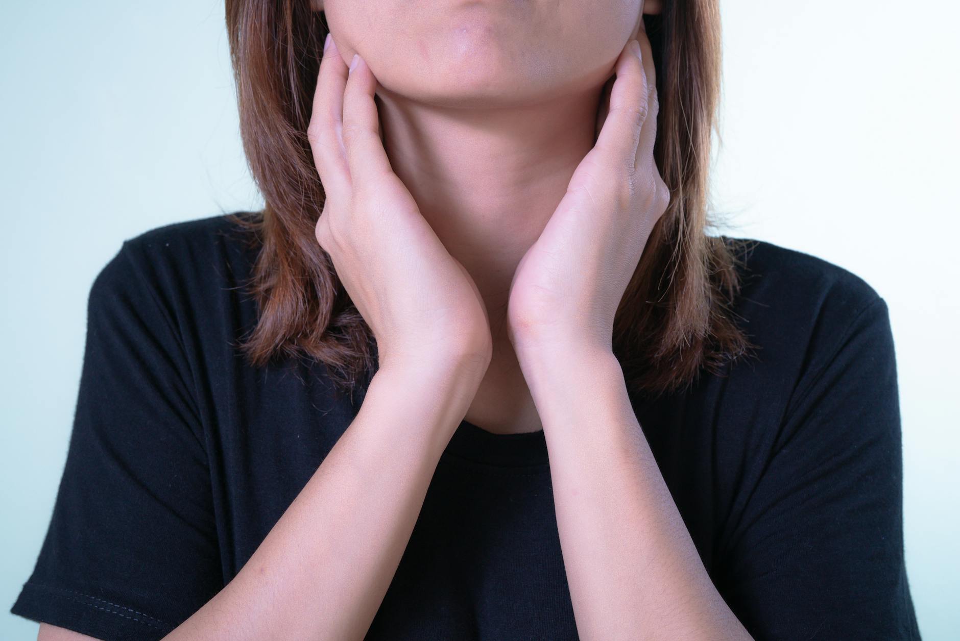 Close-up of a woman touching her neck, possibly indicating discomfort or throat pain. - relationship anxiety symptoms