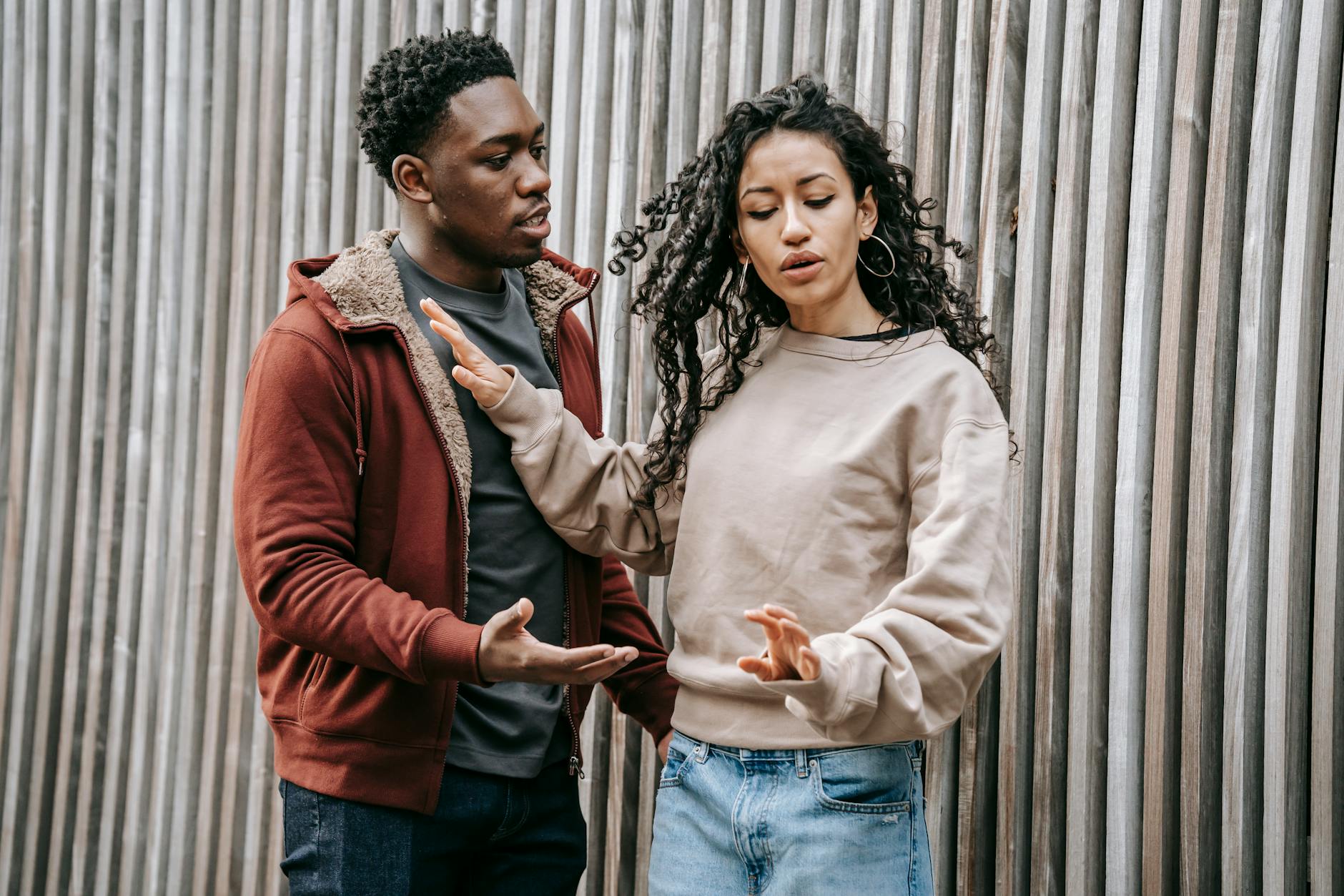 A diverse couple expressing conflict and disagreement outside against a wooden fence. - relationship conflict resolution