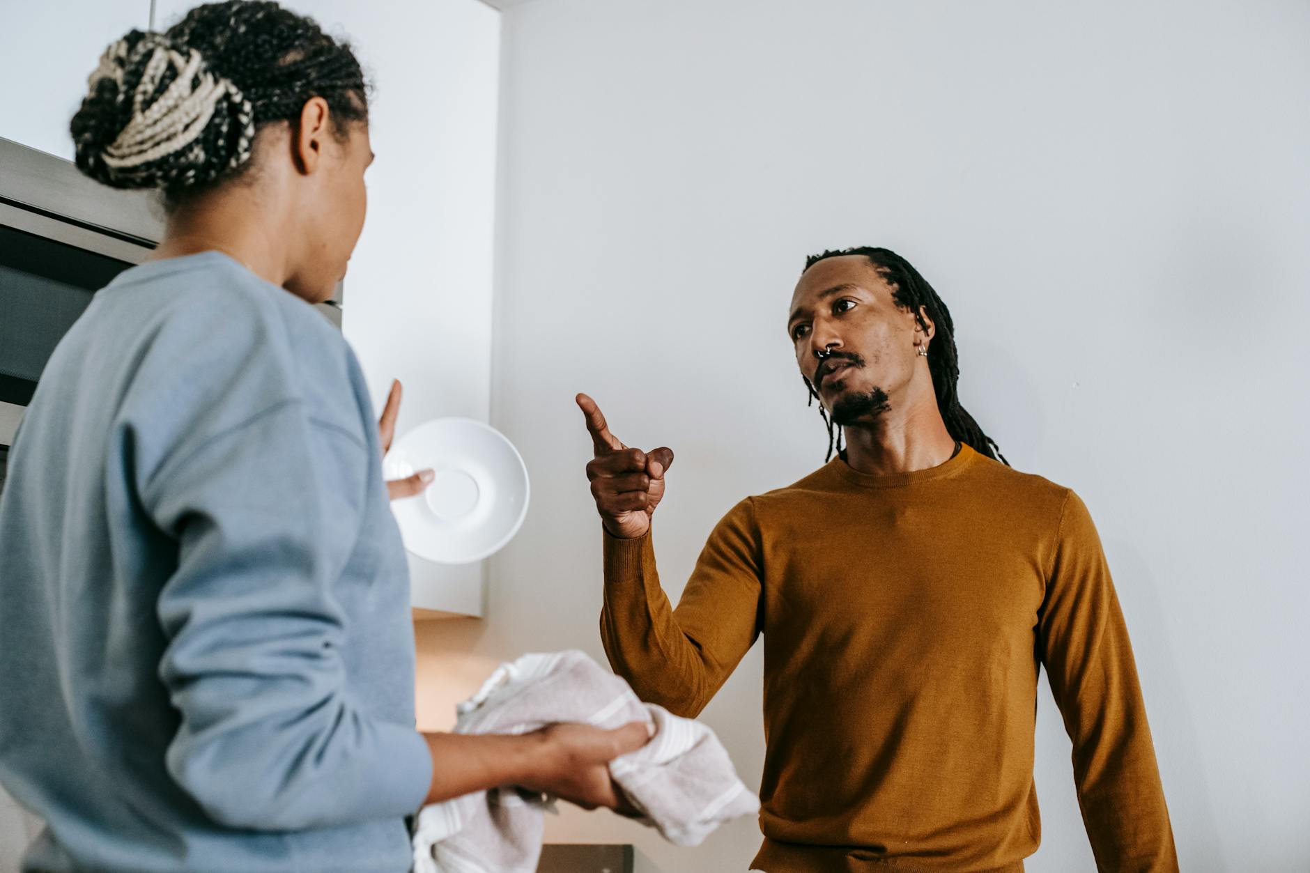 Annoyed African American male with finger up menacing to anonymous female partner while arguing in kitchen and looking at each other - relationship conflict resolution