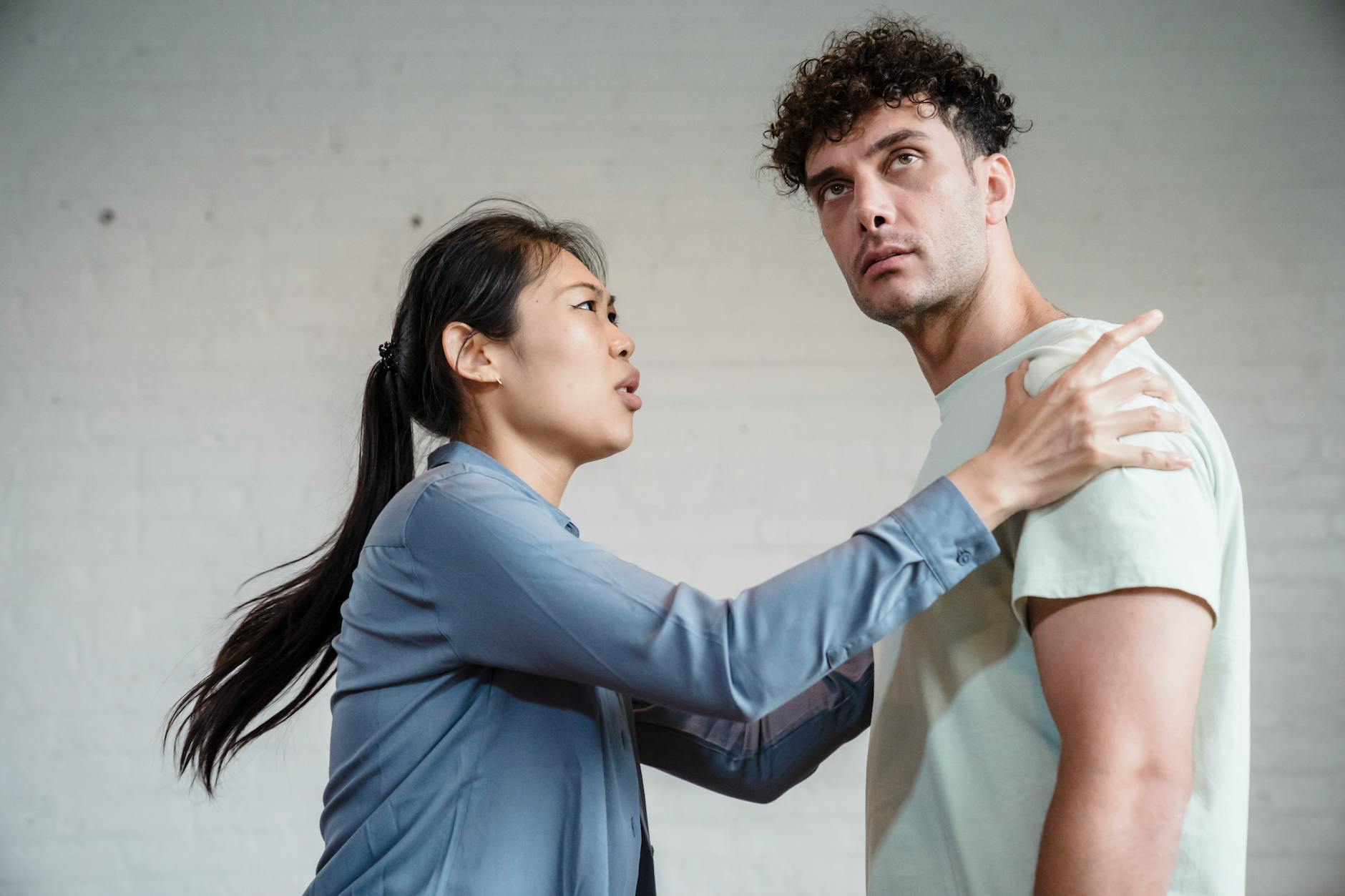 An Asian woman and Caucasian man engaged in an emotional discussion against a brick wall. - relationship conflict resolution