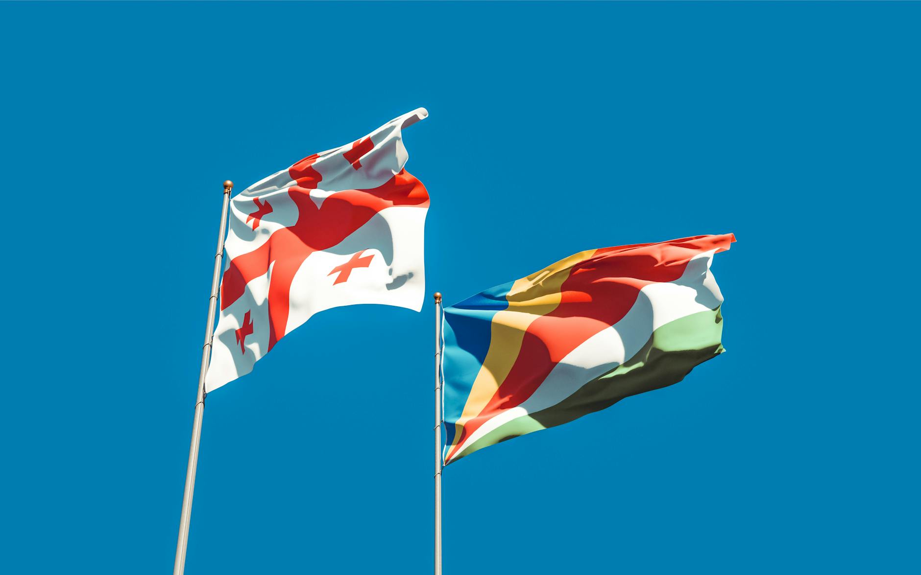 Vibrant image of Georgia and Seychelles flags waving with blue sky backdrop, symbolizing unity and cultural pride. - relationship red flags