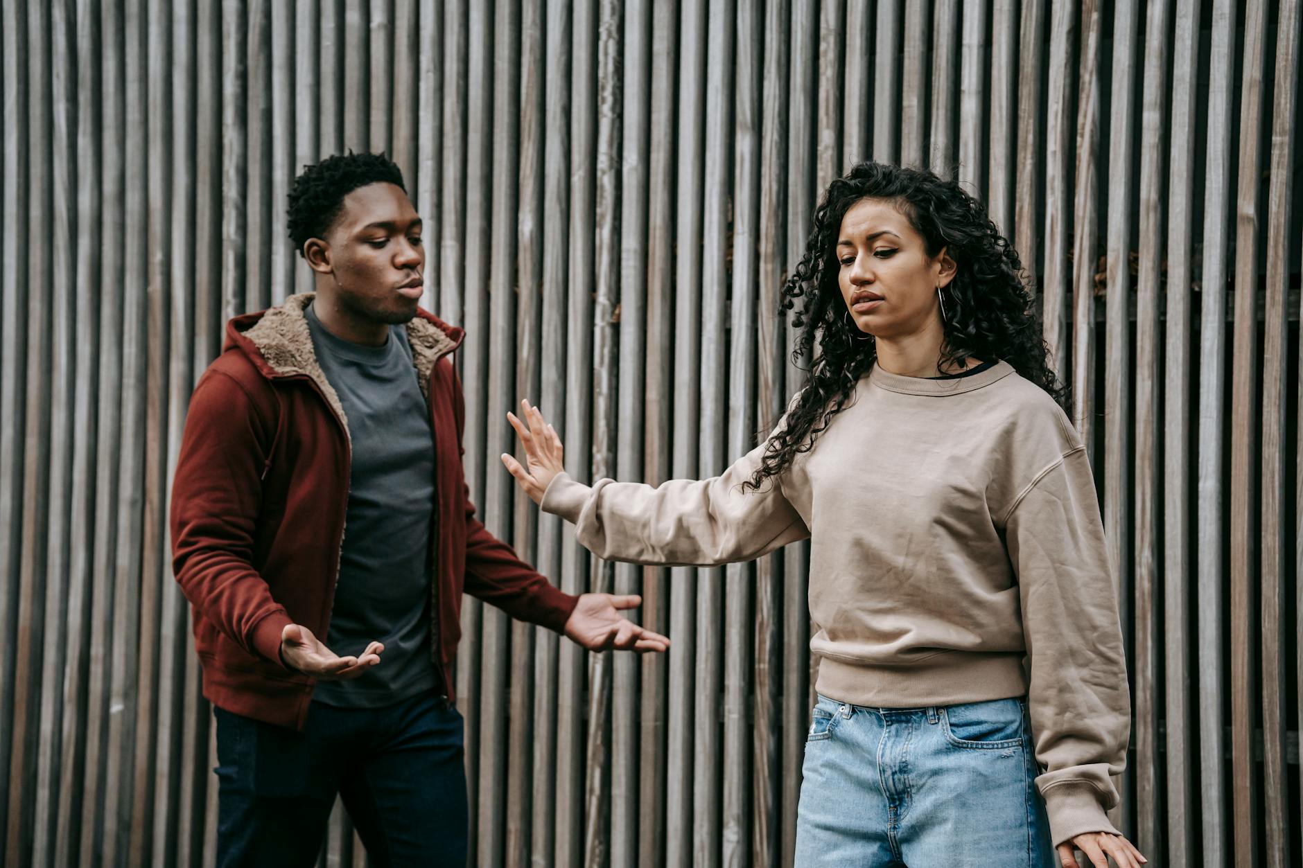 Insulted ethnic girlfriend with outstretched arm and irritated African American boyfriend having quarrel near wooden wall on street during breakup - resolve vacation disagreements
