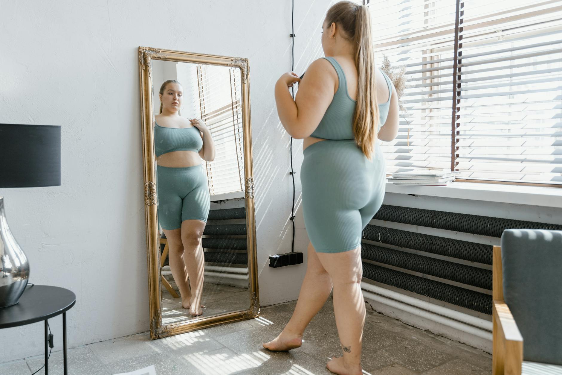 Plus size woman in activewear admiring her reflection in a mirror indoors. - self esteem building exercises