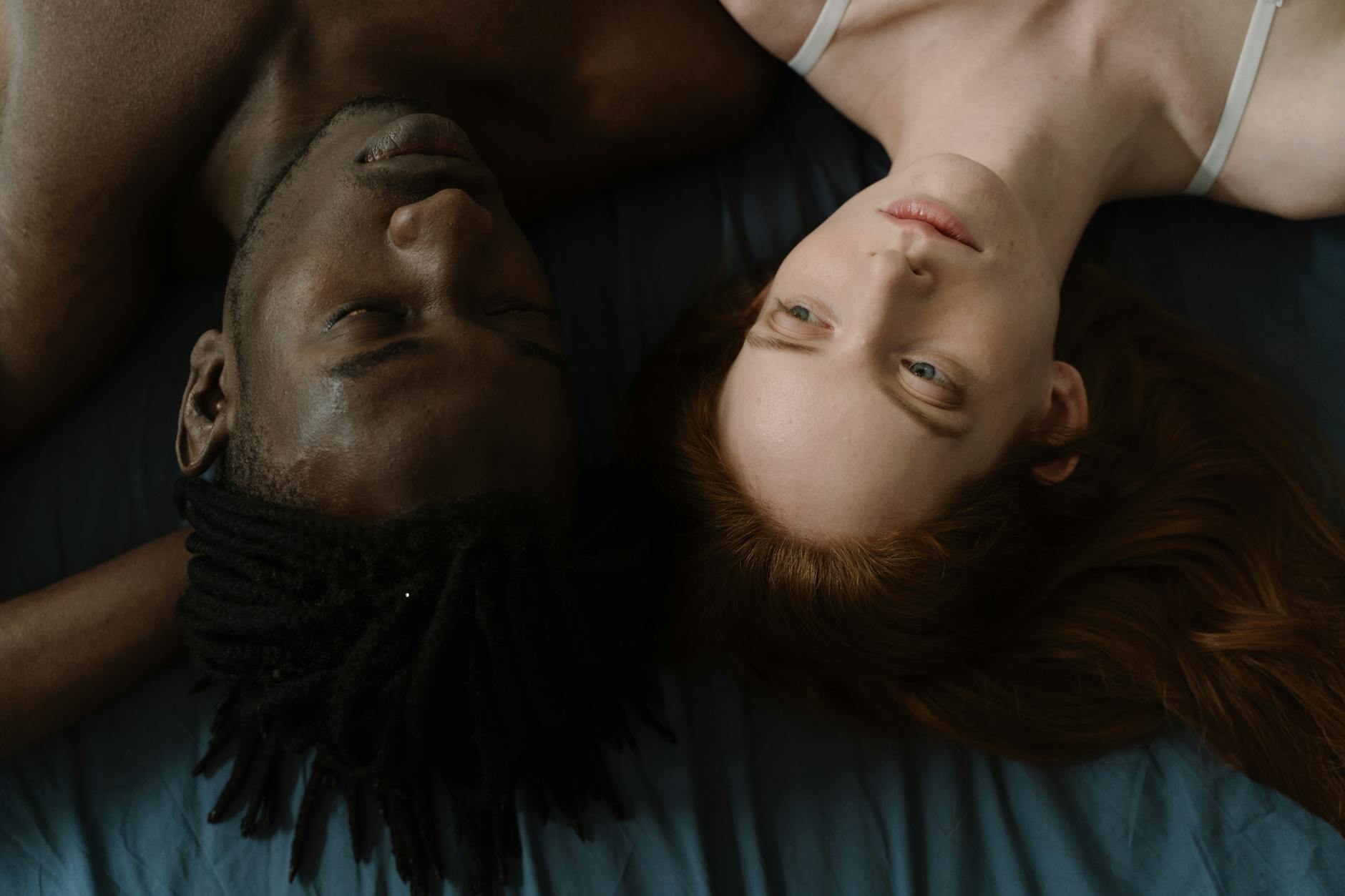 Top view of a serene interracial couple lying side by side on a bed, embracing love and intimacy. - shared relationship goals