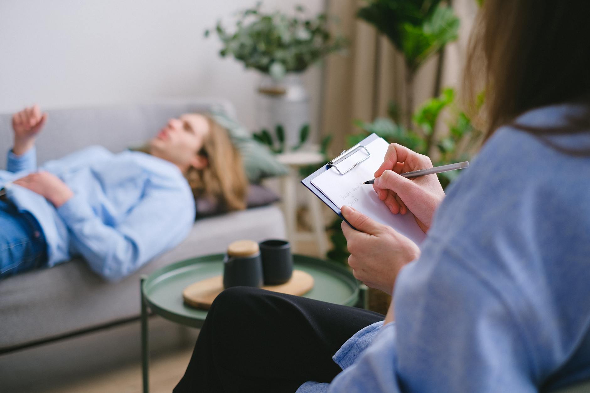 A therapy session in progress with a therapist taking notes as a patient reclines on a sofa. - therapy for commitment issues