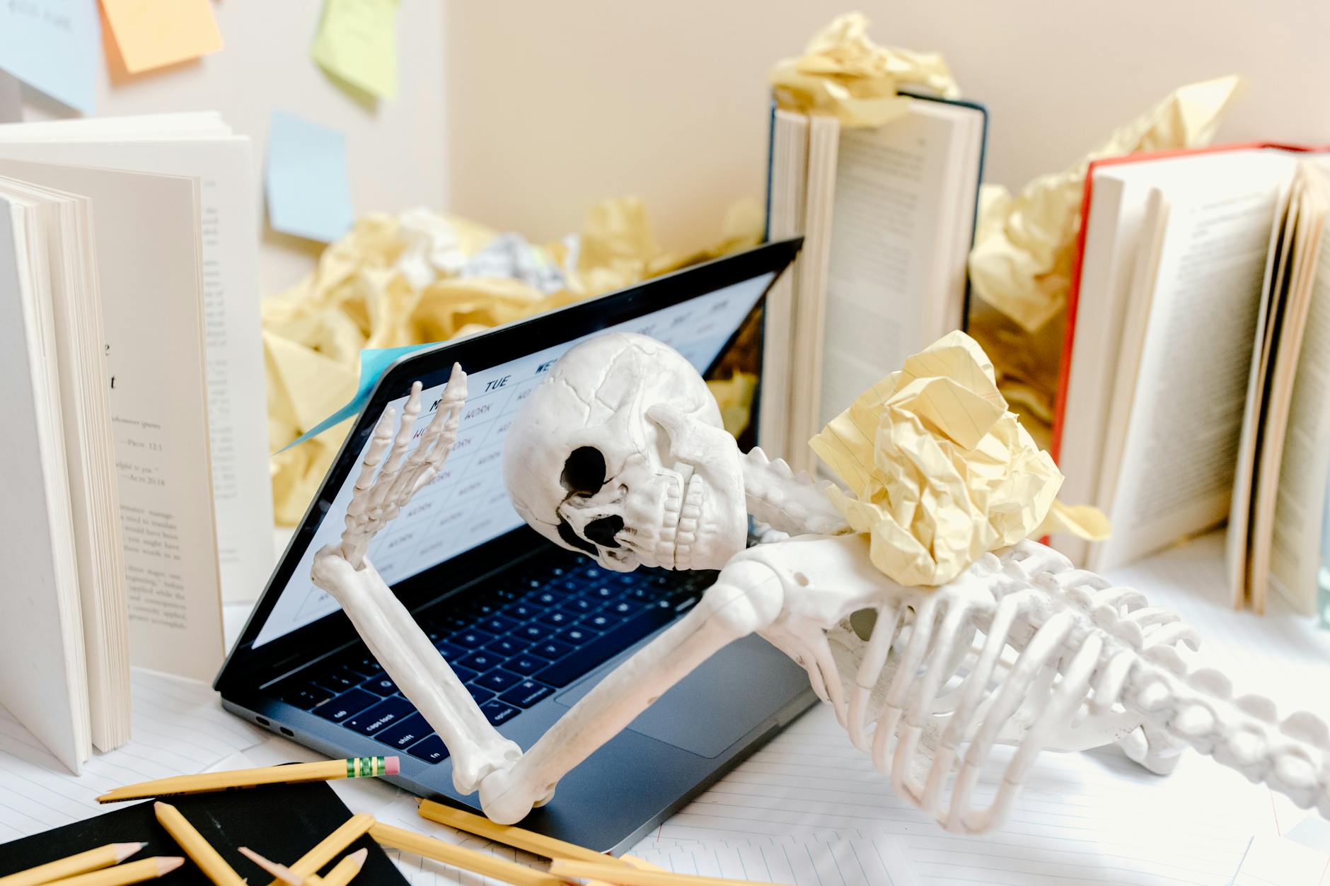 A skeleton surrounded by crumpled paper and books at a messy desk symbolizes burnout and overwork. - therapy for winter slump