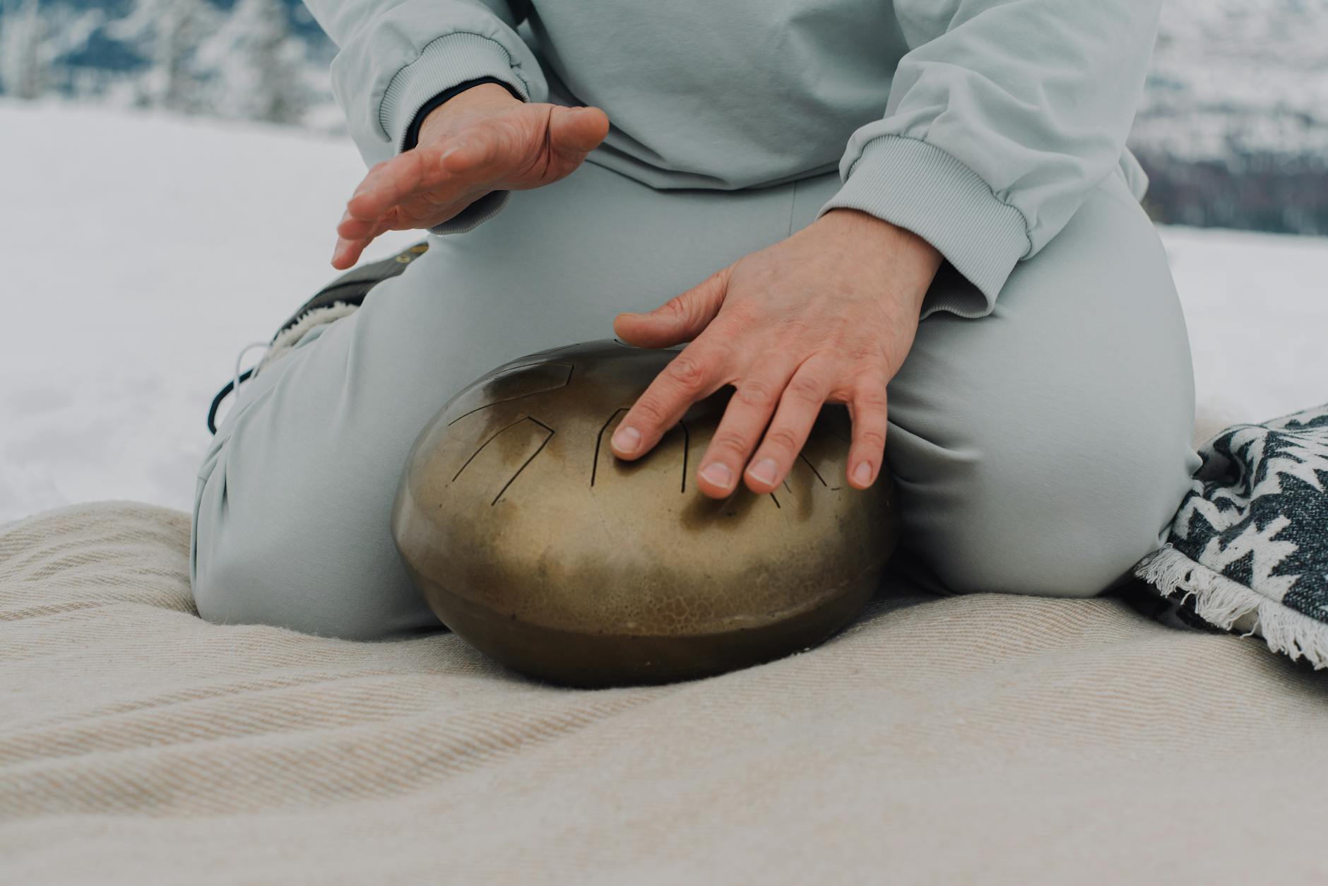 Hands tapping a steel tongue drum outdoors on a snowy winter day. - therapy for winter slump