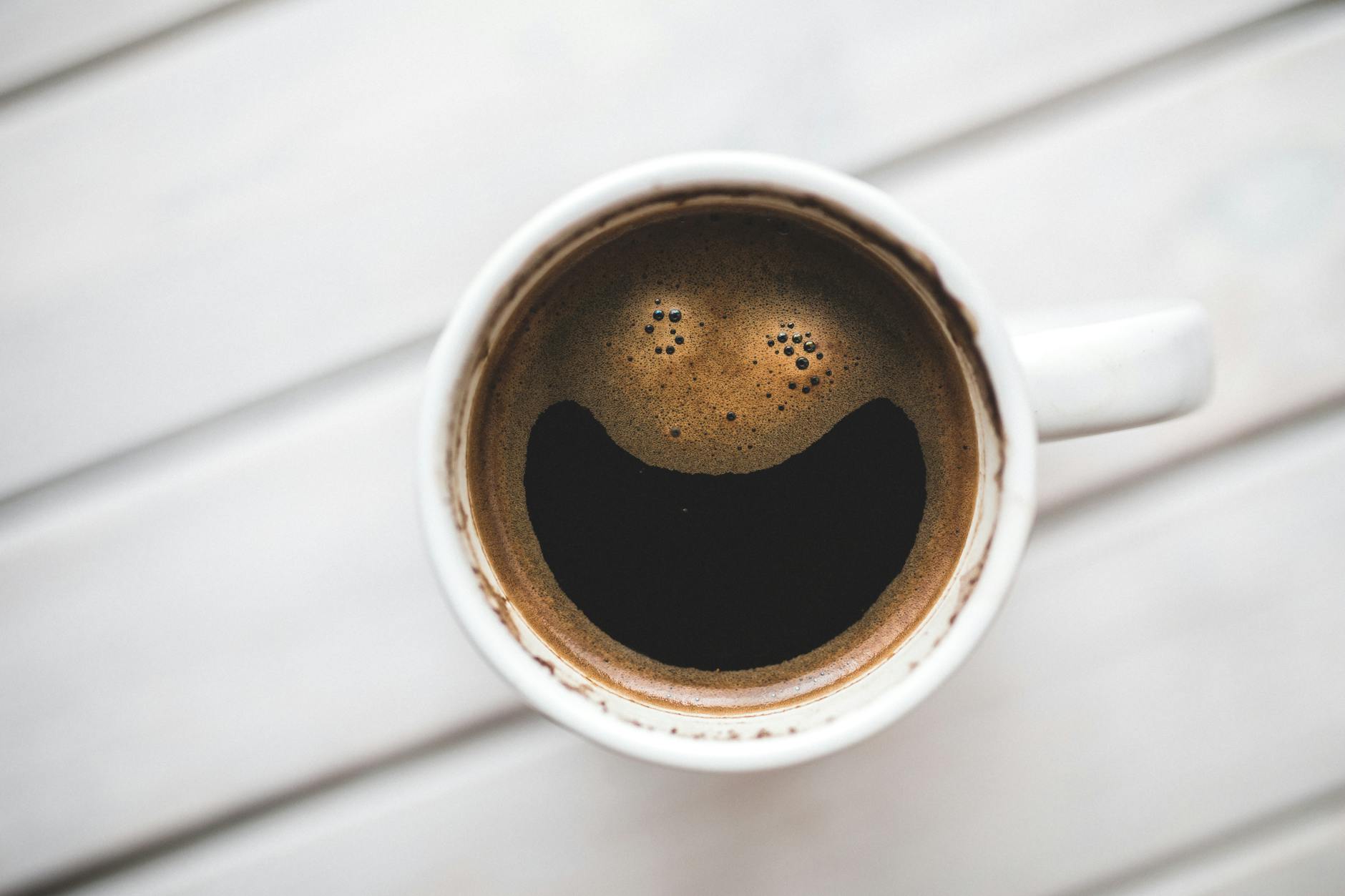 A coffee cup with a smiling face pattern on a wooden table, perfect for morning routines. - winter mood boosting tips
