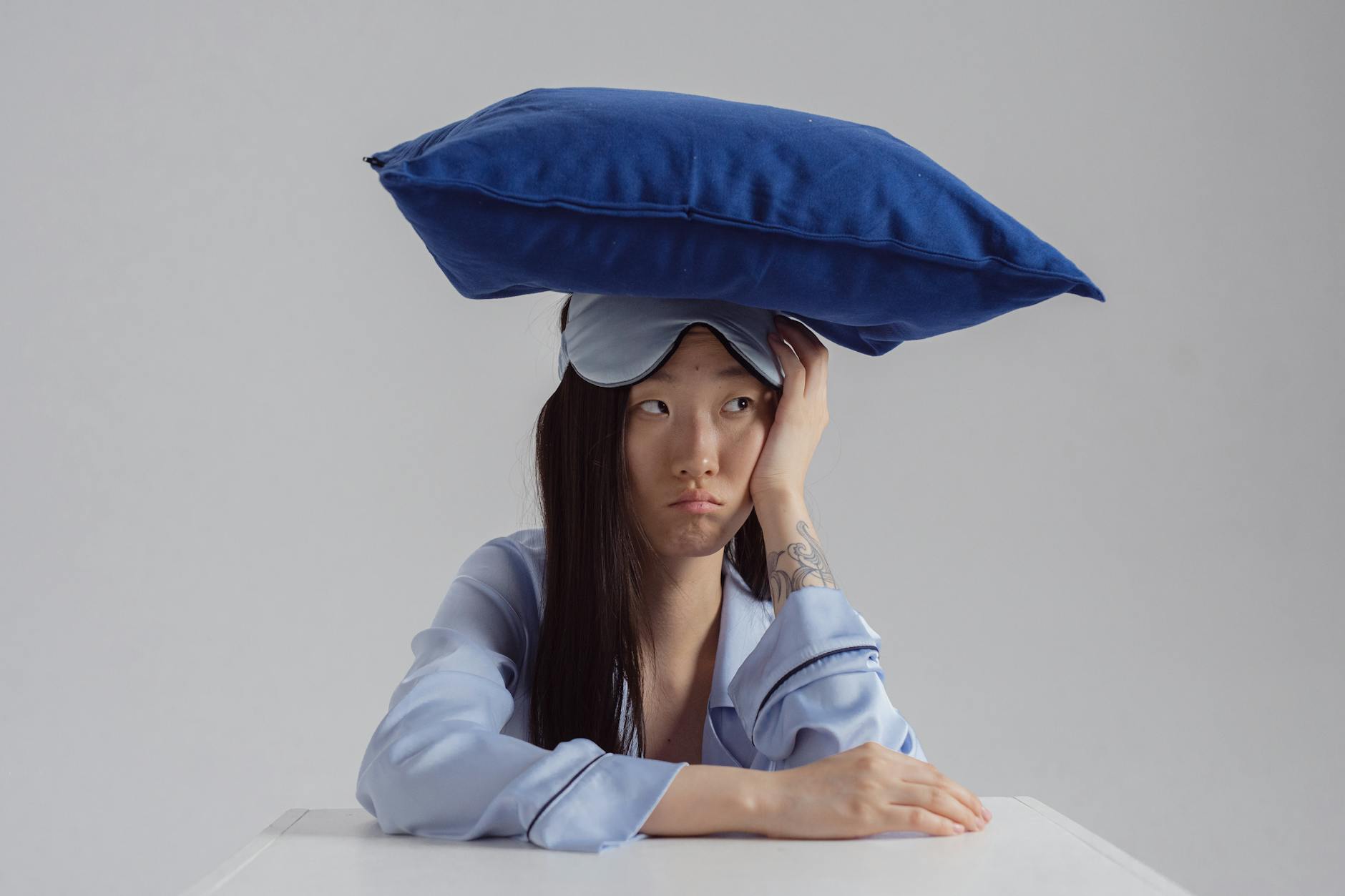 Tattooed woman with pillow and sleep mask showing insomnia concept. - winter sleep problems