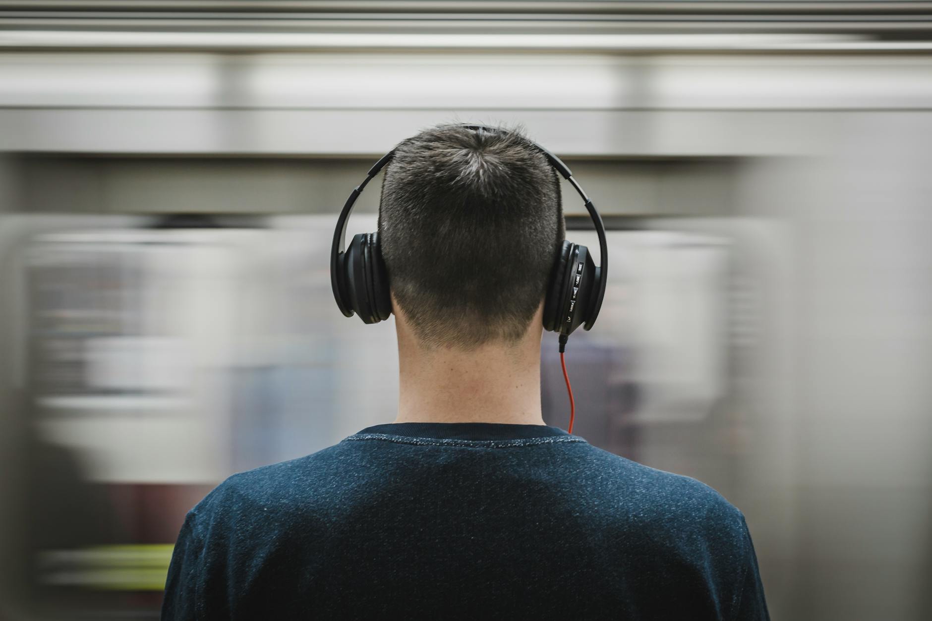 Rear view of a man with headphones standing at a subway platform, blurred train passing by. - active listening importance