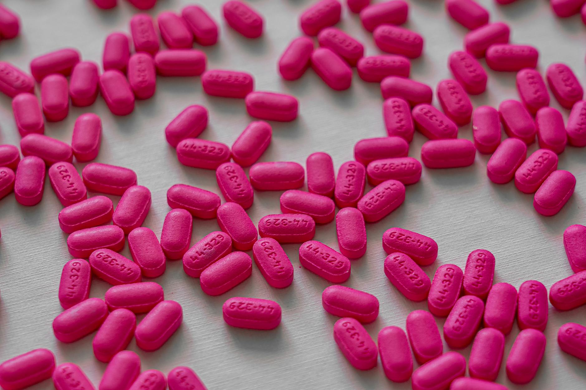 Close-up view of pink tablets scattered on a white table for medication and health treatment. - allergy mental health