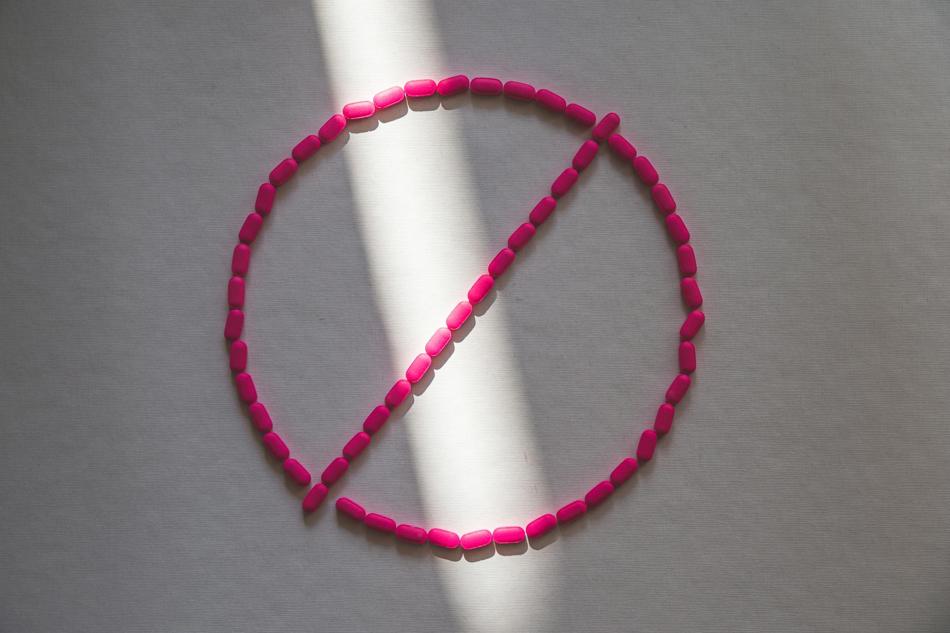 Pink pills arranged in a prohibition symbol in sunlight, symbolizing drug restrictions. - allergy mental health