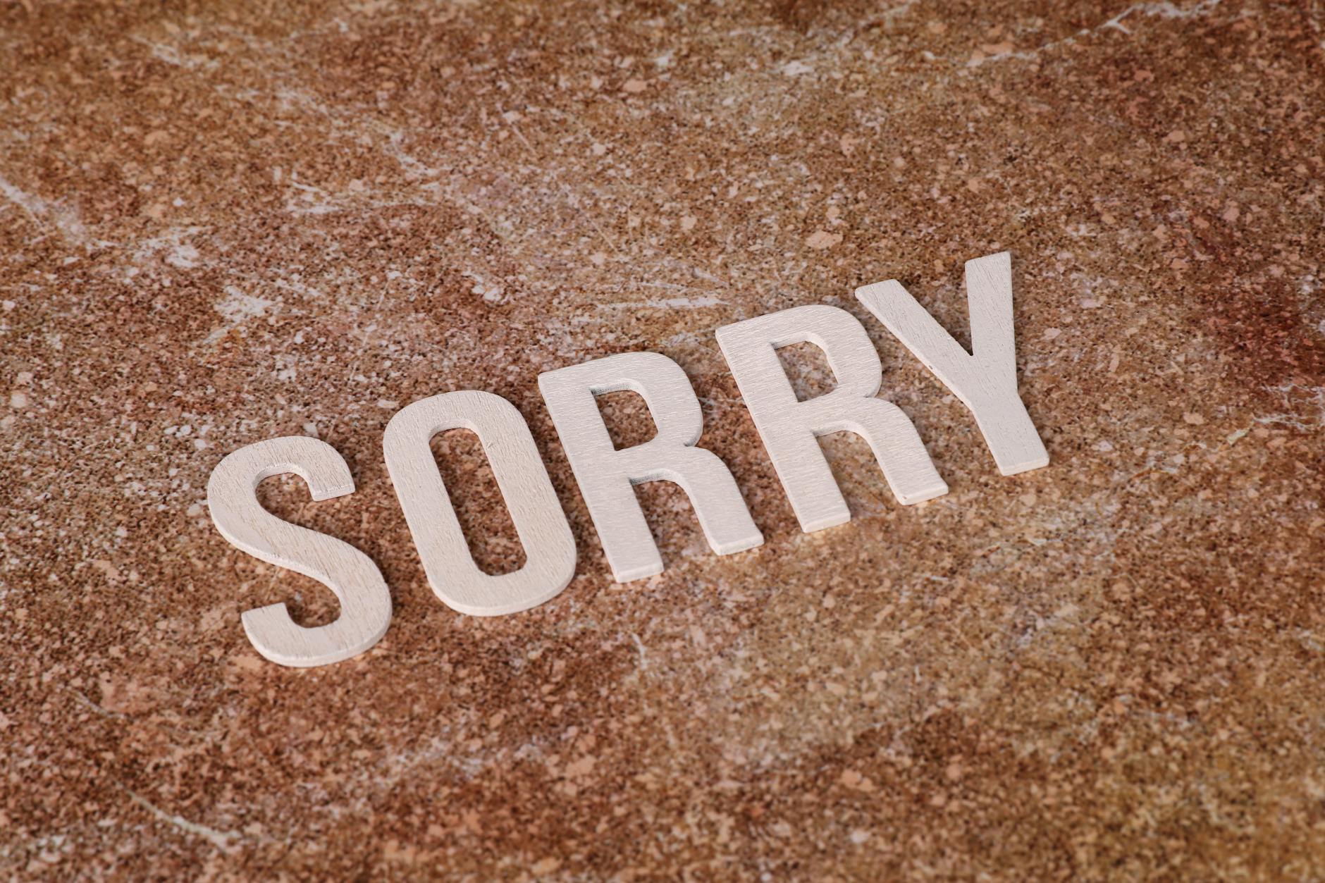 Wooden letters spelling 'SORRY' on a textured marble surface, symbolizing apology or regret. - how to apologize
