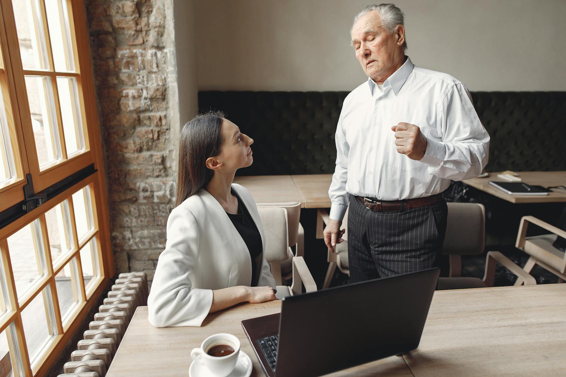 Two professionals engage in a serious discussion in a modern office with natural lighting and warm tones. - assertive communication examples